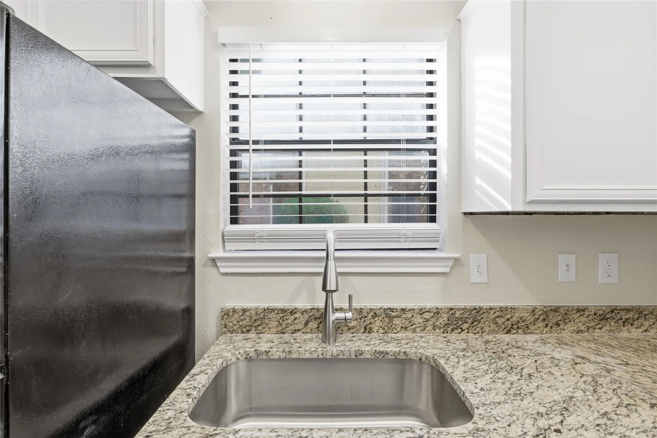 Stainless steel sink with a gooseneck faucet, light-toned granite countertops, and white upper cabinetry