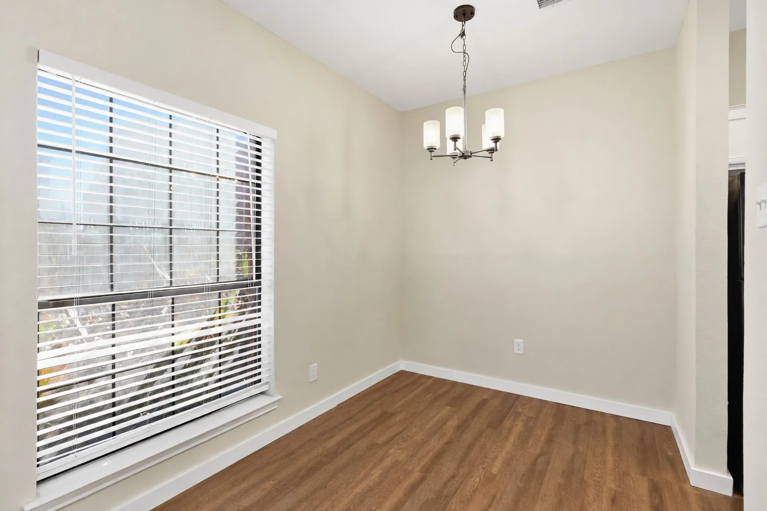 Natural light from a prominent window, wood-finish flooring, neutral wall tones, white trim, and a contemporary chandelier