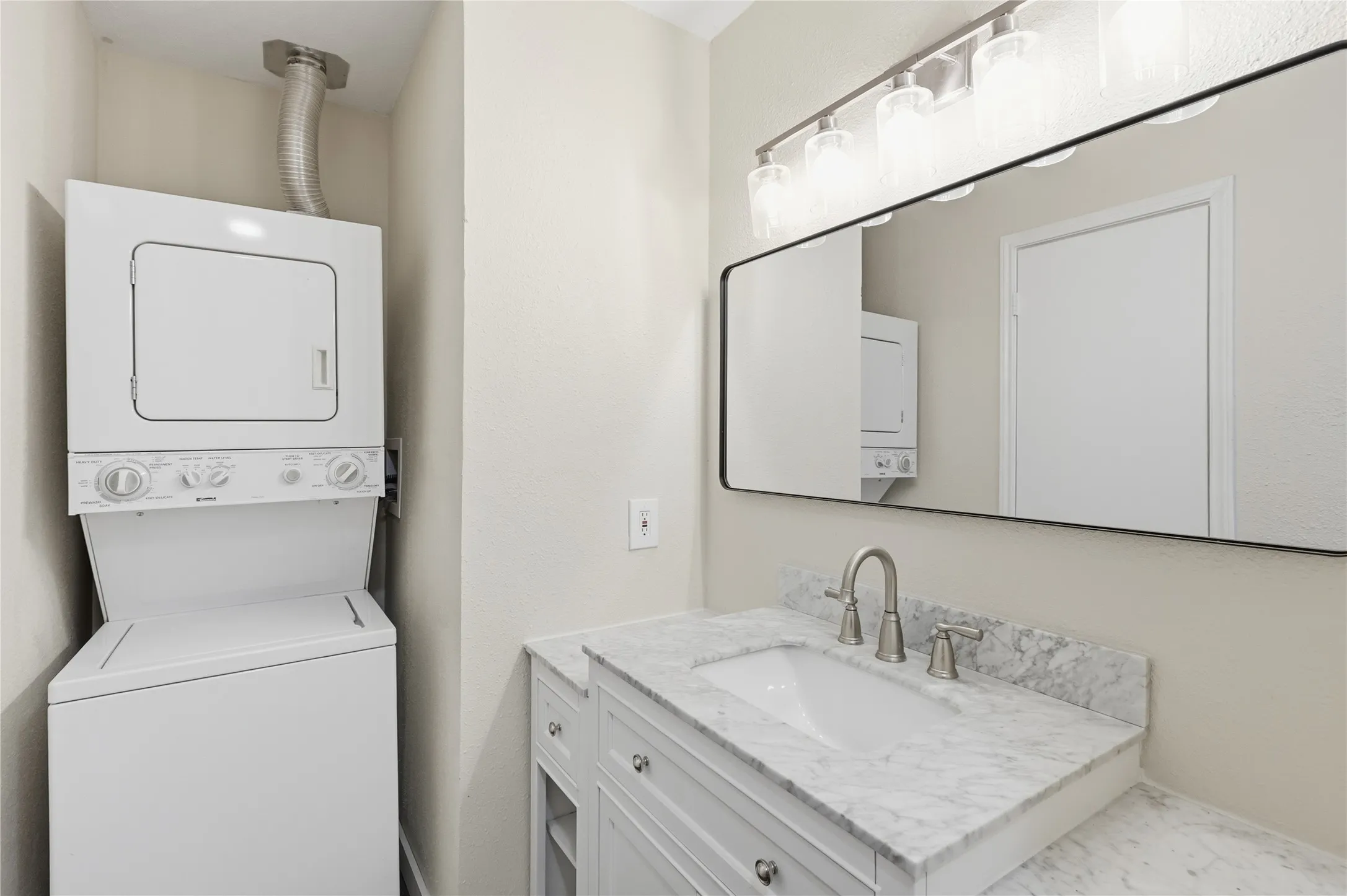 Laundry stackable unit, vanity with integrated sink, stone countertop, brushed nickel faucet, and a rectangular framed mirror