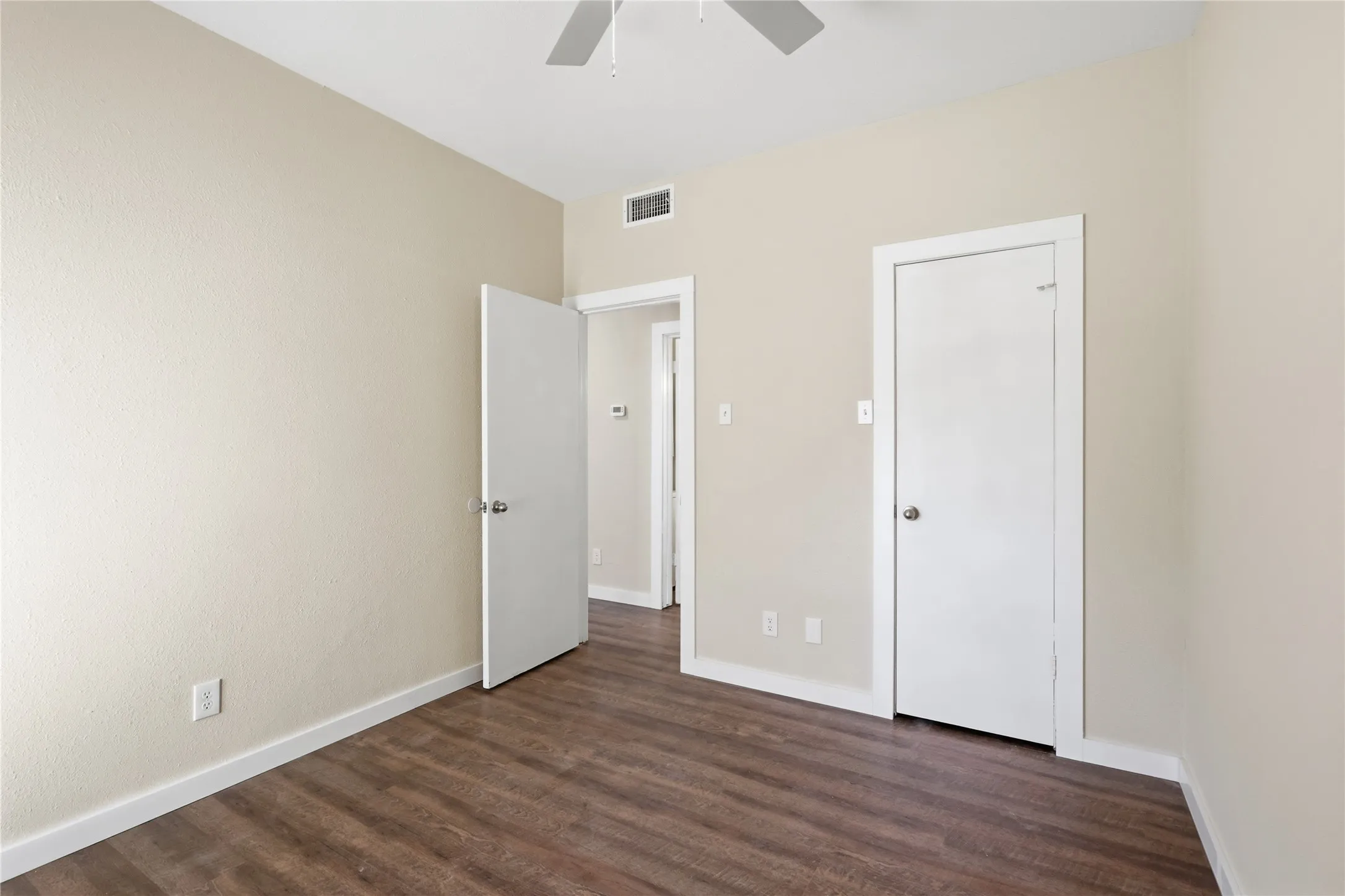 Wood-finish flooring, neutral wall tones, white trim details, ceiling fan, and white interior doors