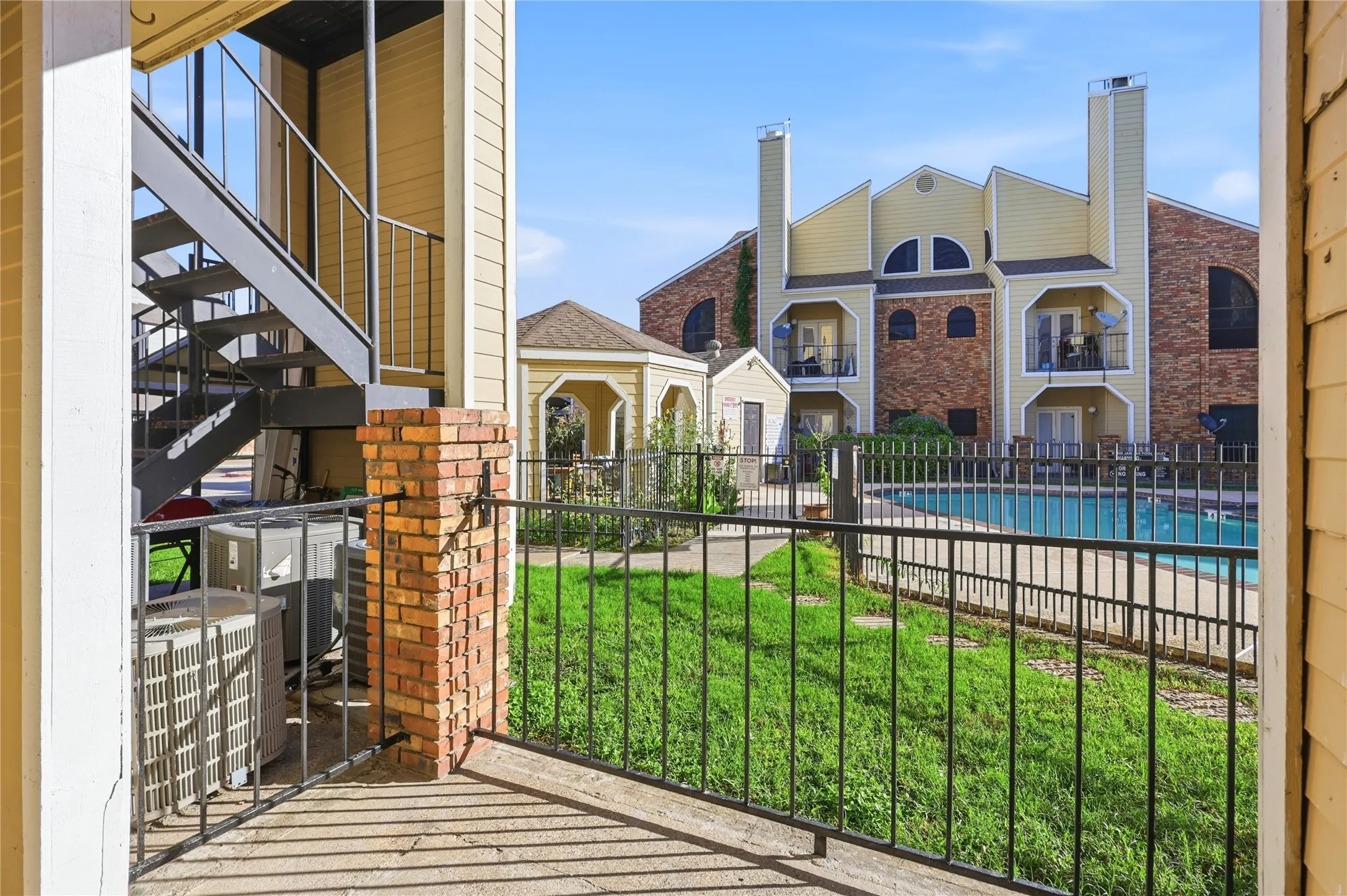 Patio with brick pillar accents and black metal railing overlooking a fenced swimming pool, central gazebo, and landscaped green space