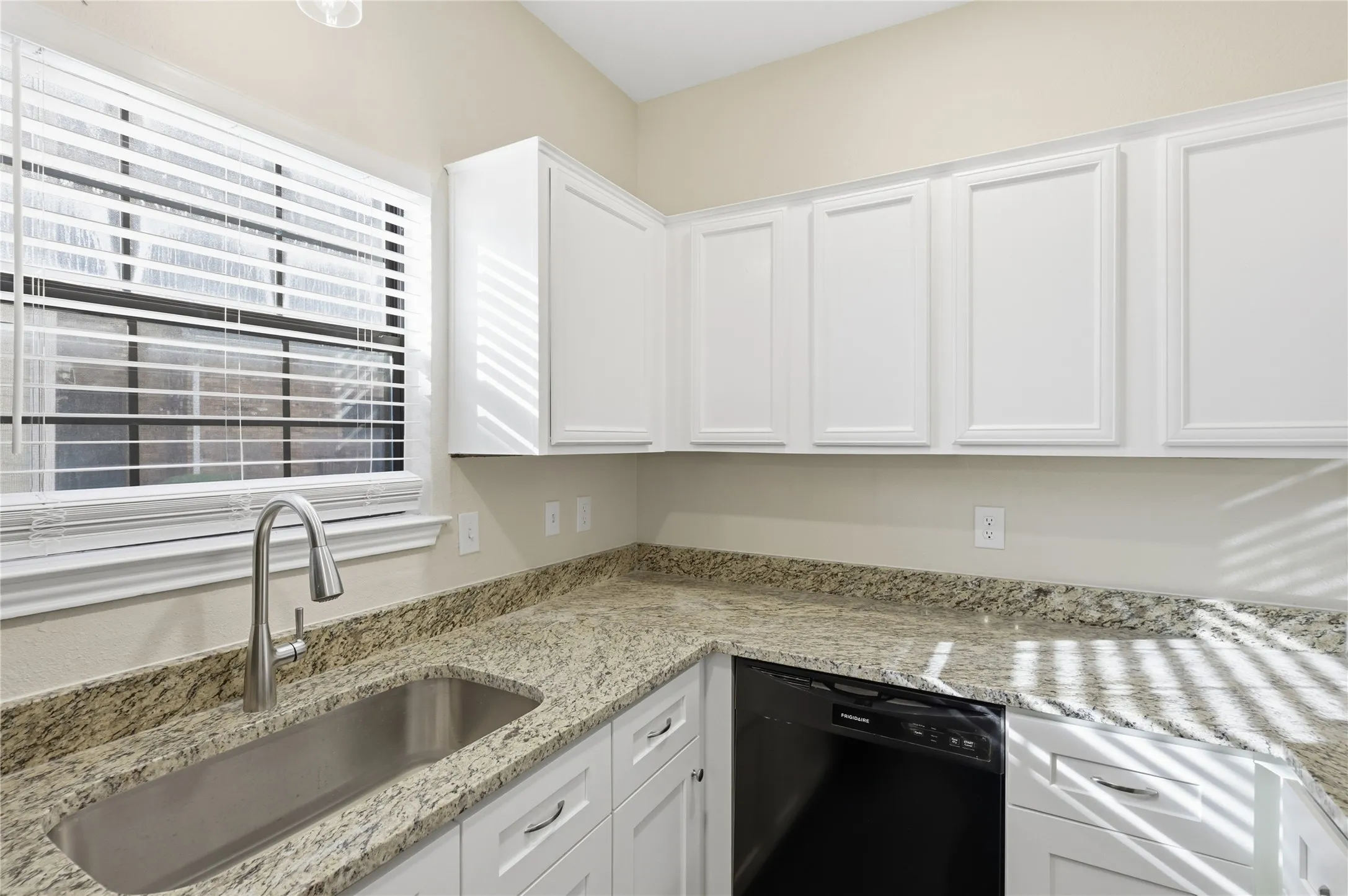 White shaker-style cabinetry, granite countertops, undermount stainless steel sink, gooseneck faucet, and a black dishwasher