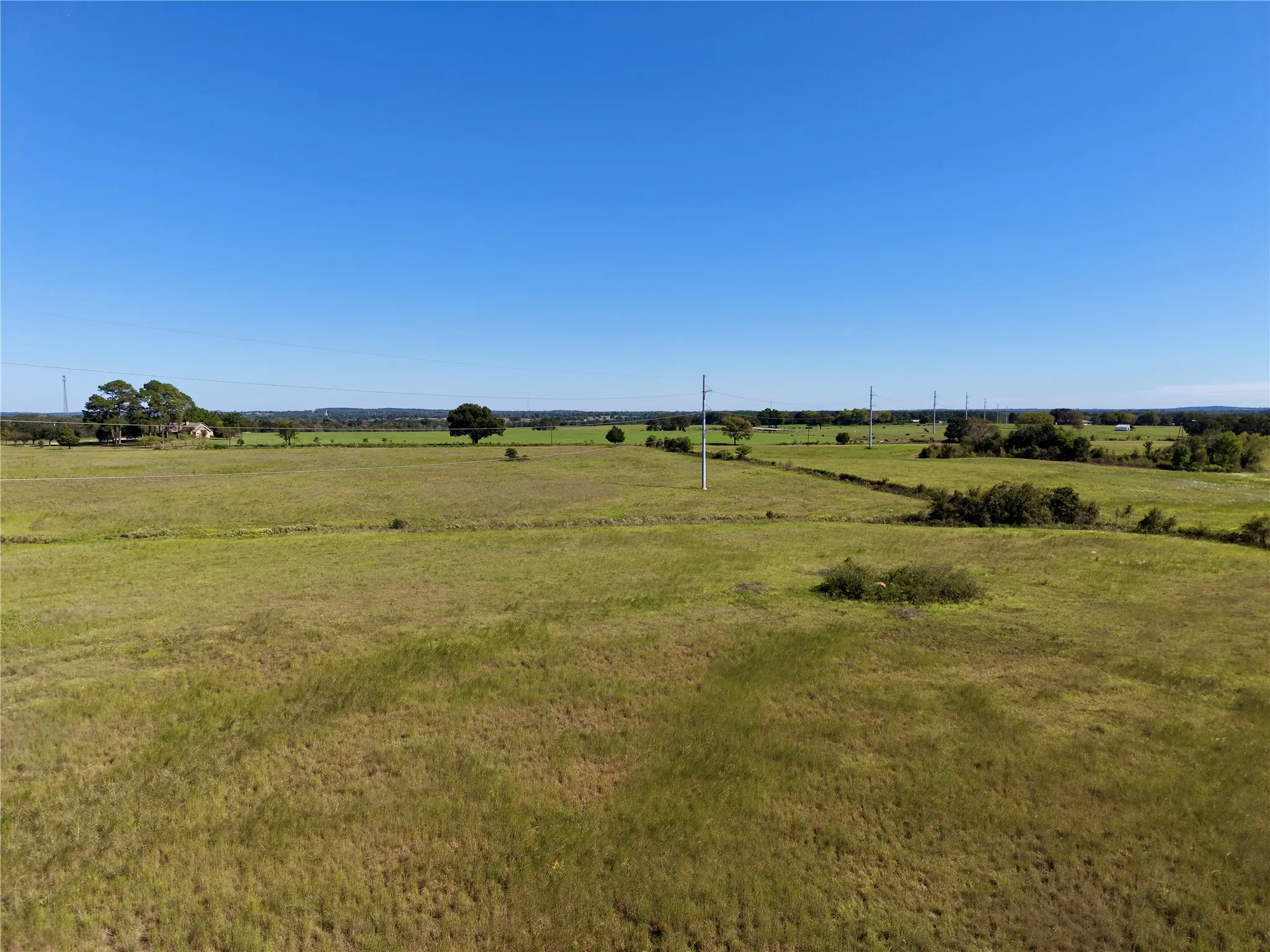Elevated view of open ground, scattered trees and the transmission corridor.