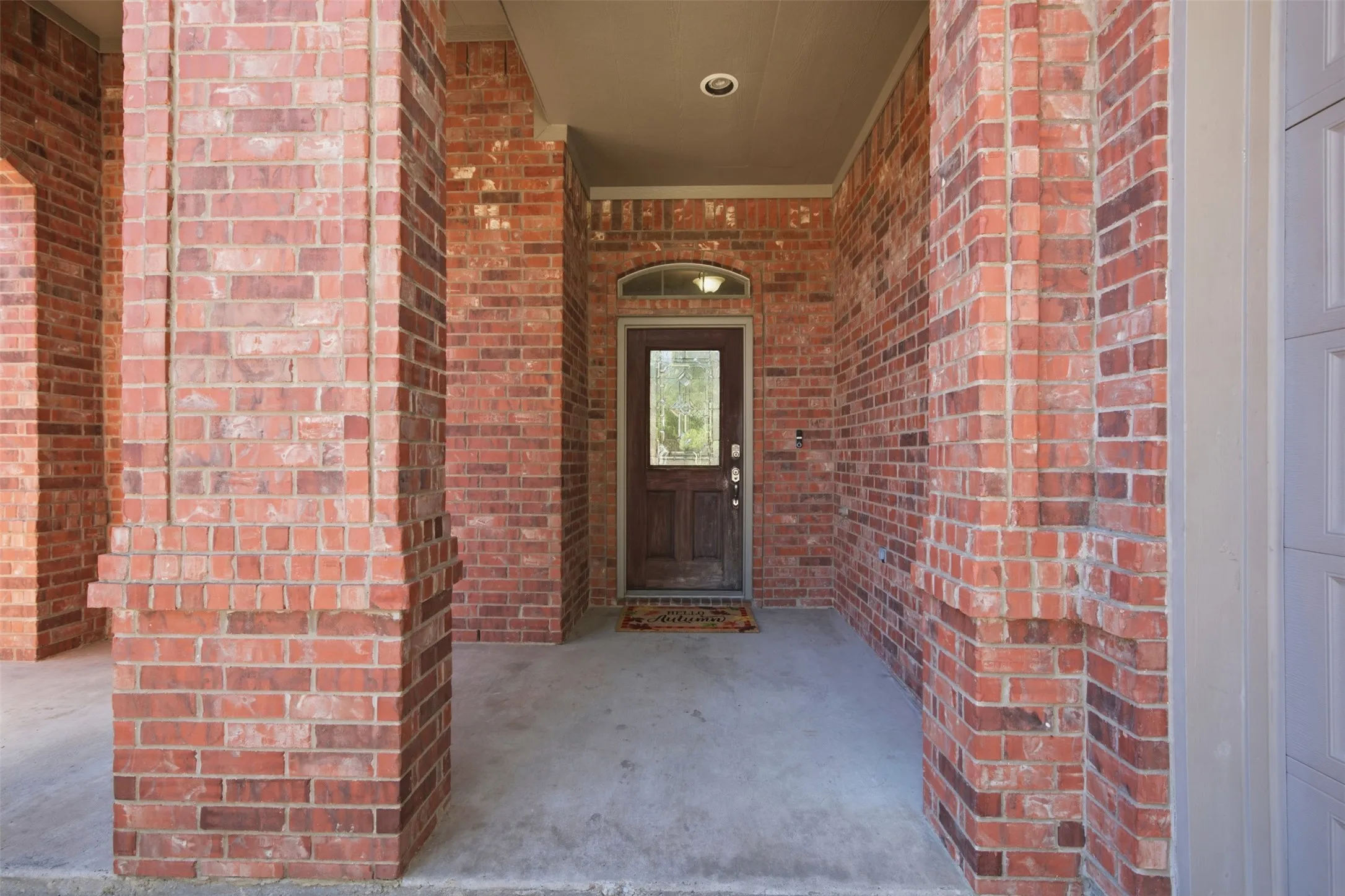 Brick exterior with decorative brick columns, covered concrete entry, recessed lighting, and a wood-panel entry door with an arched transom window
