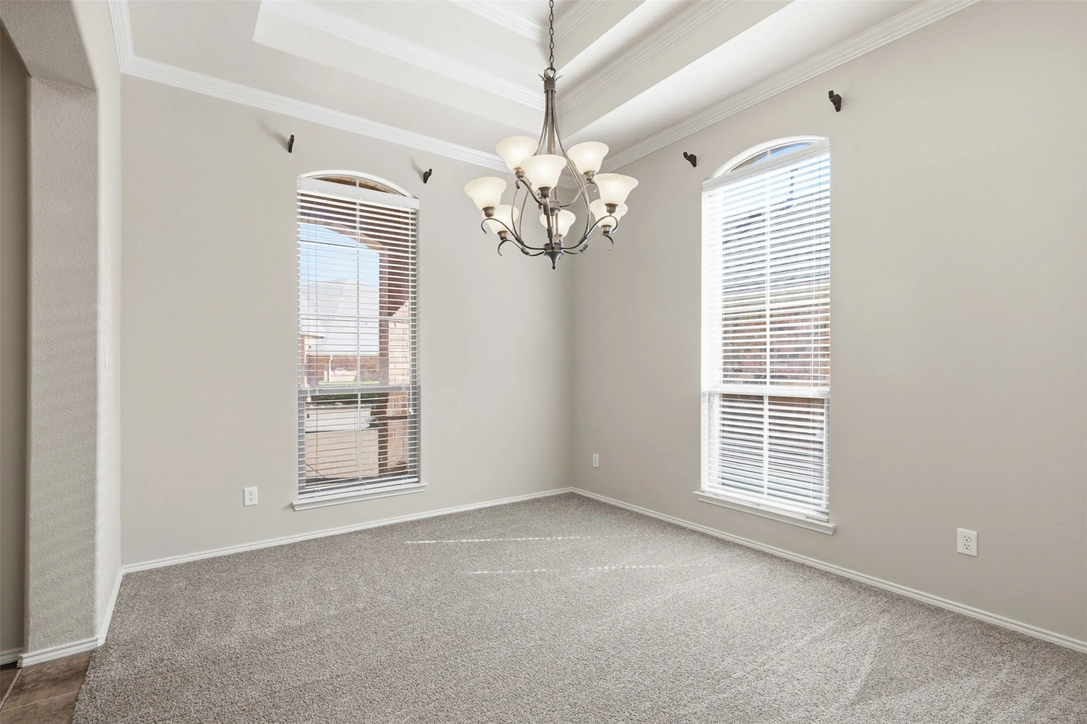 Tray ceiling with crown molding, chandelier lighting, two arched windows with blinds, and carpet flooring