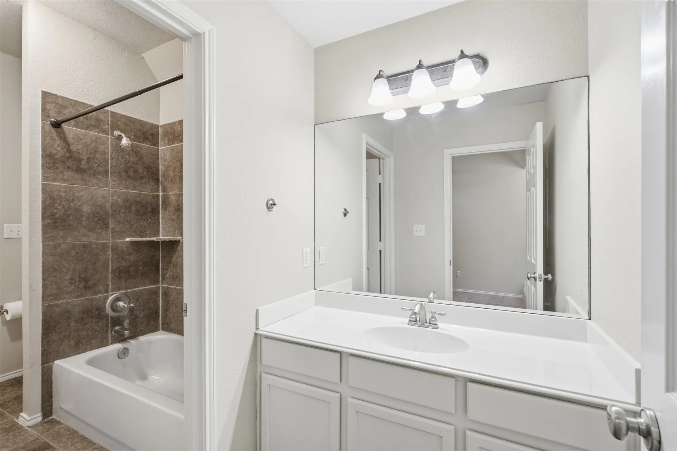 Full vanity mirror, white flat-panel cabinetry, white countertop, integrated sink, and tub-shower combination with tiled surround
