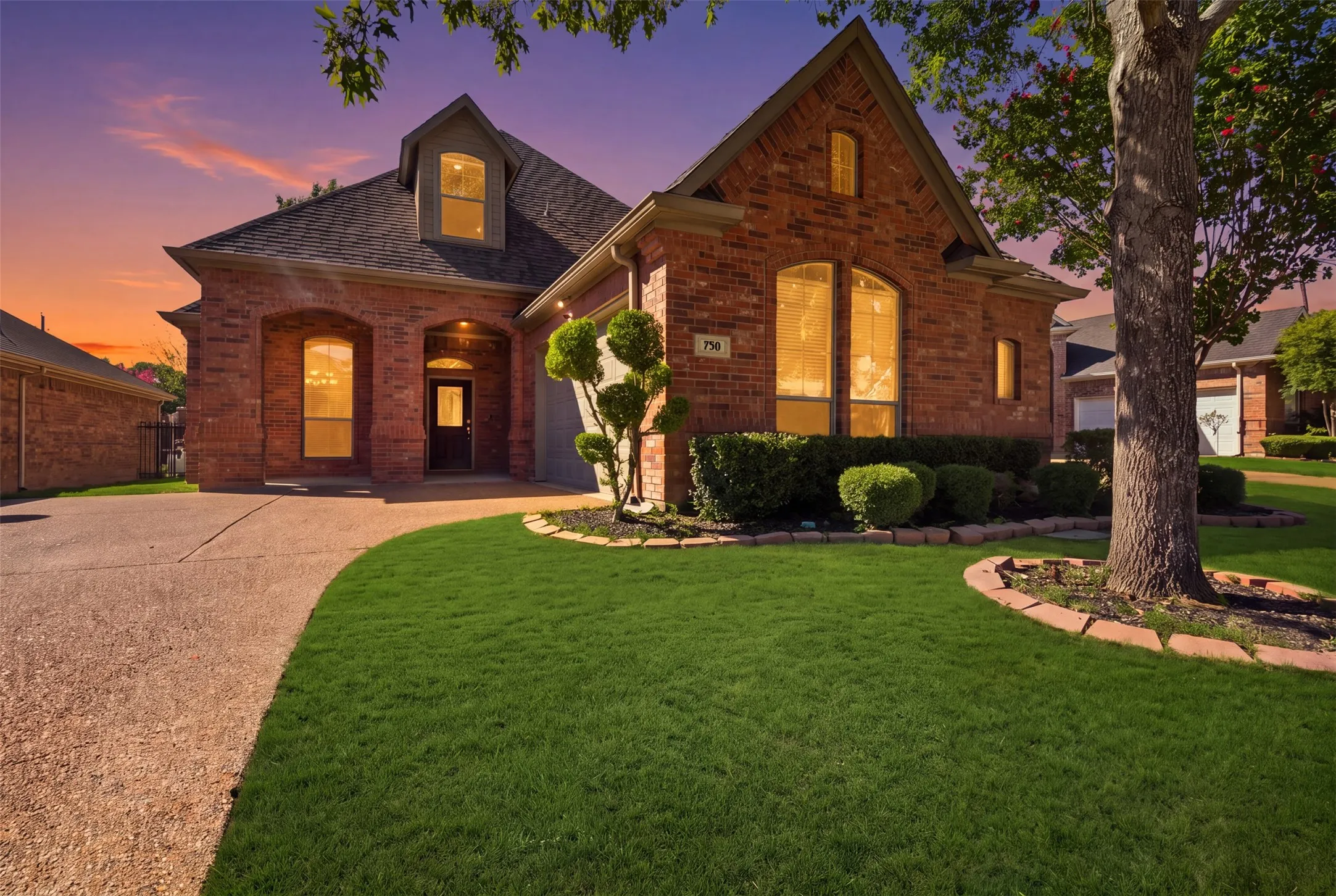 Brick exterior with arched entryways, gabled roofline, dormer window, and mature landscaping. Green enhancement to lawn.
