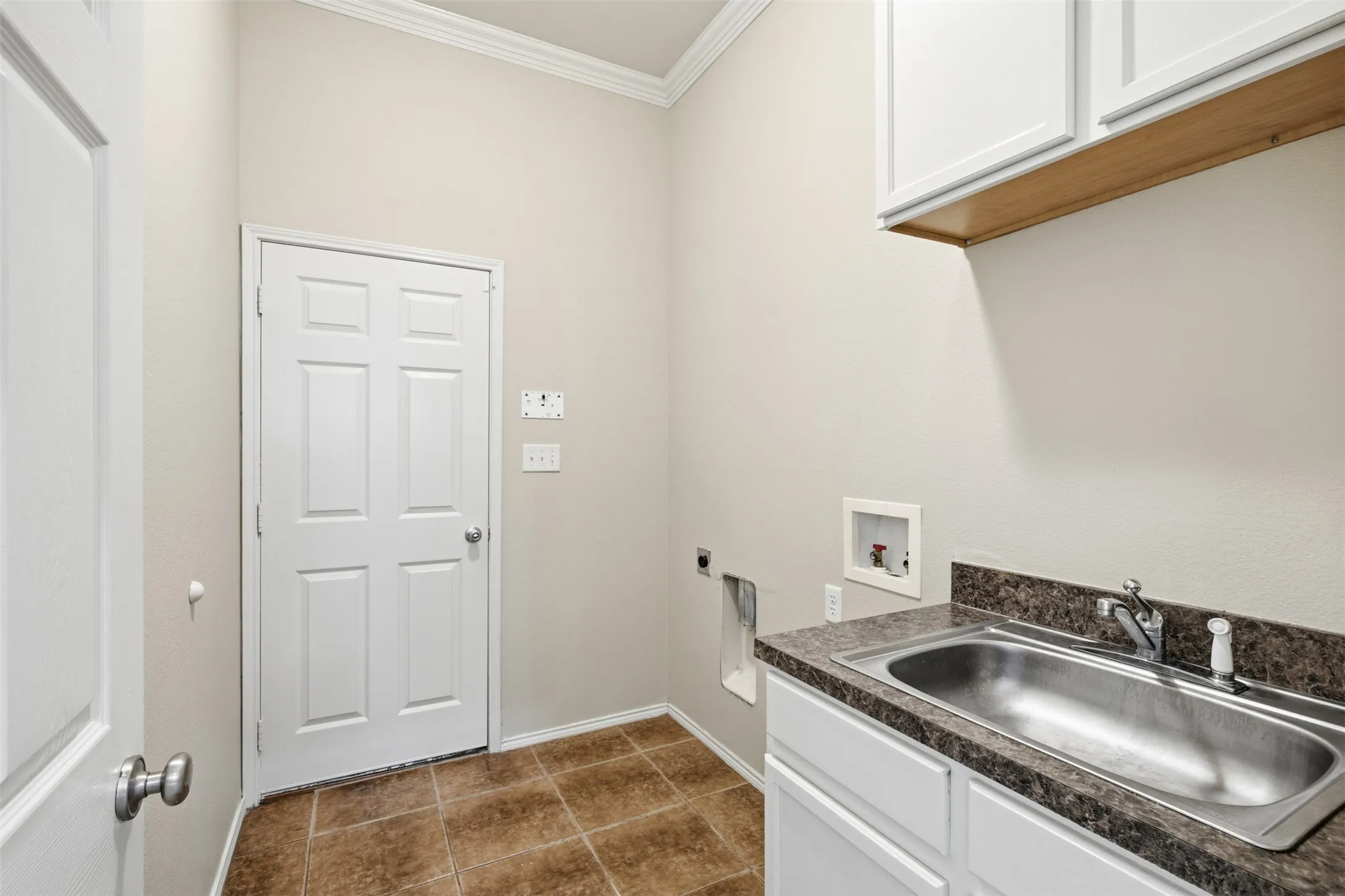 Laundry area featuring a utility sink, white cabinetry, and tiled flooring
