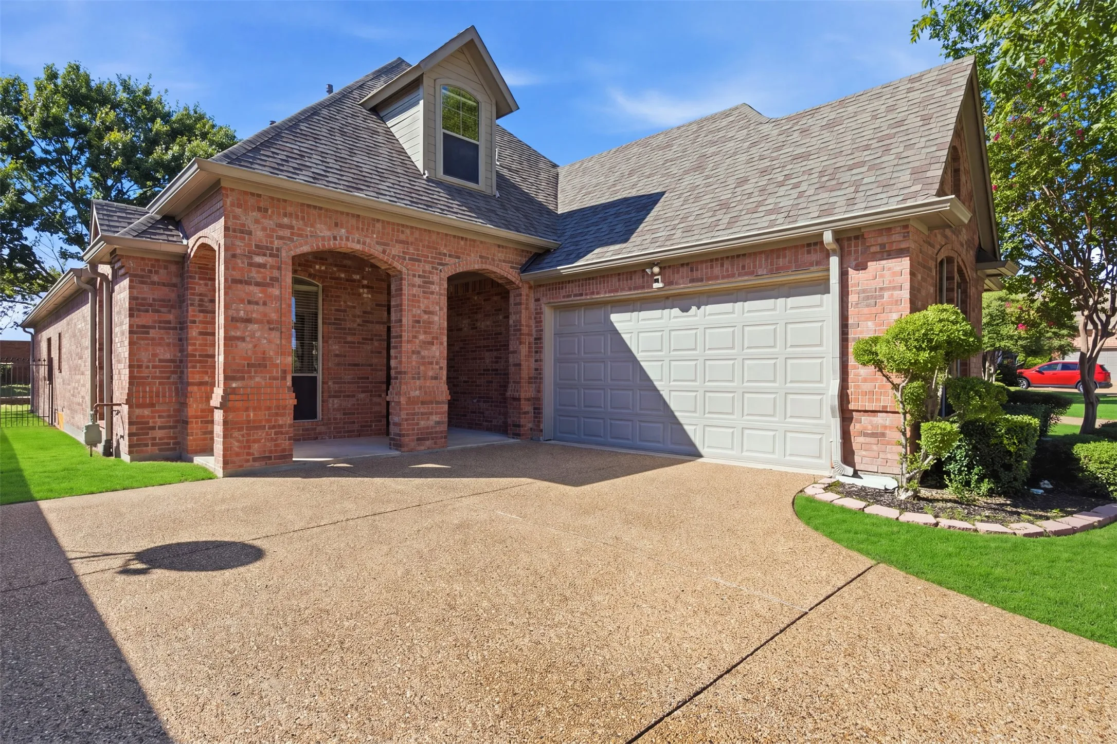 Red brick exterior with an arched entryway, gabled roof, and attached garage. Green enhancement to lawn.