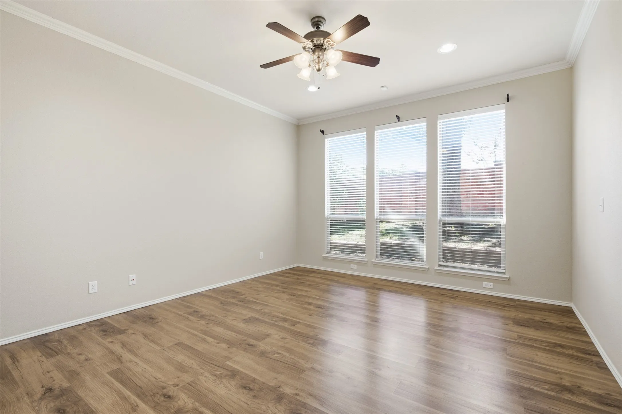 Wood-finish flooring, crown molding, three large windows with blinds, ceiling fan with integrated lighting, and recessed lighting