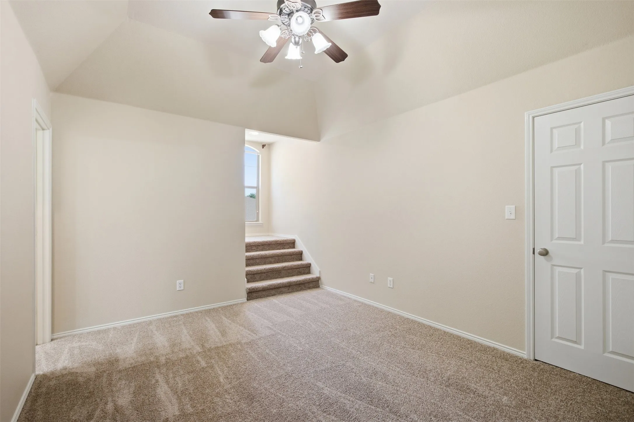Vaulted ceiling with a ceiling fan, carpeted flooring, and a paneled interior door
