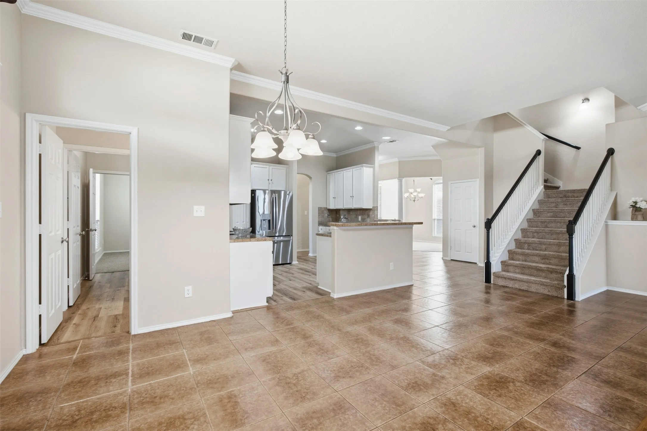 Expansive tiled flooring extending into an open-concept kitchen with white cabinetry and stainless steel appliances