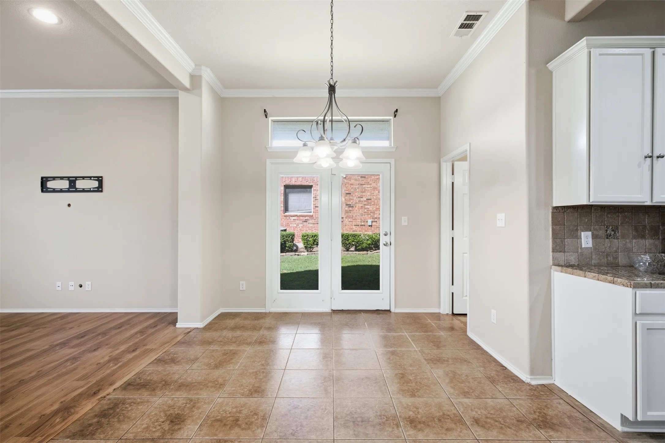 Glass-paneled door with transom window, tile flooring, wood-finish flooring, white cabinetry, and a built-in chandelier