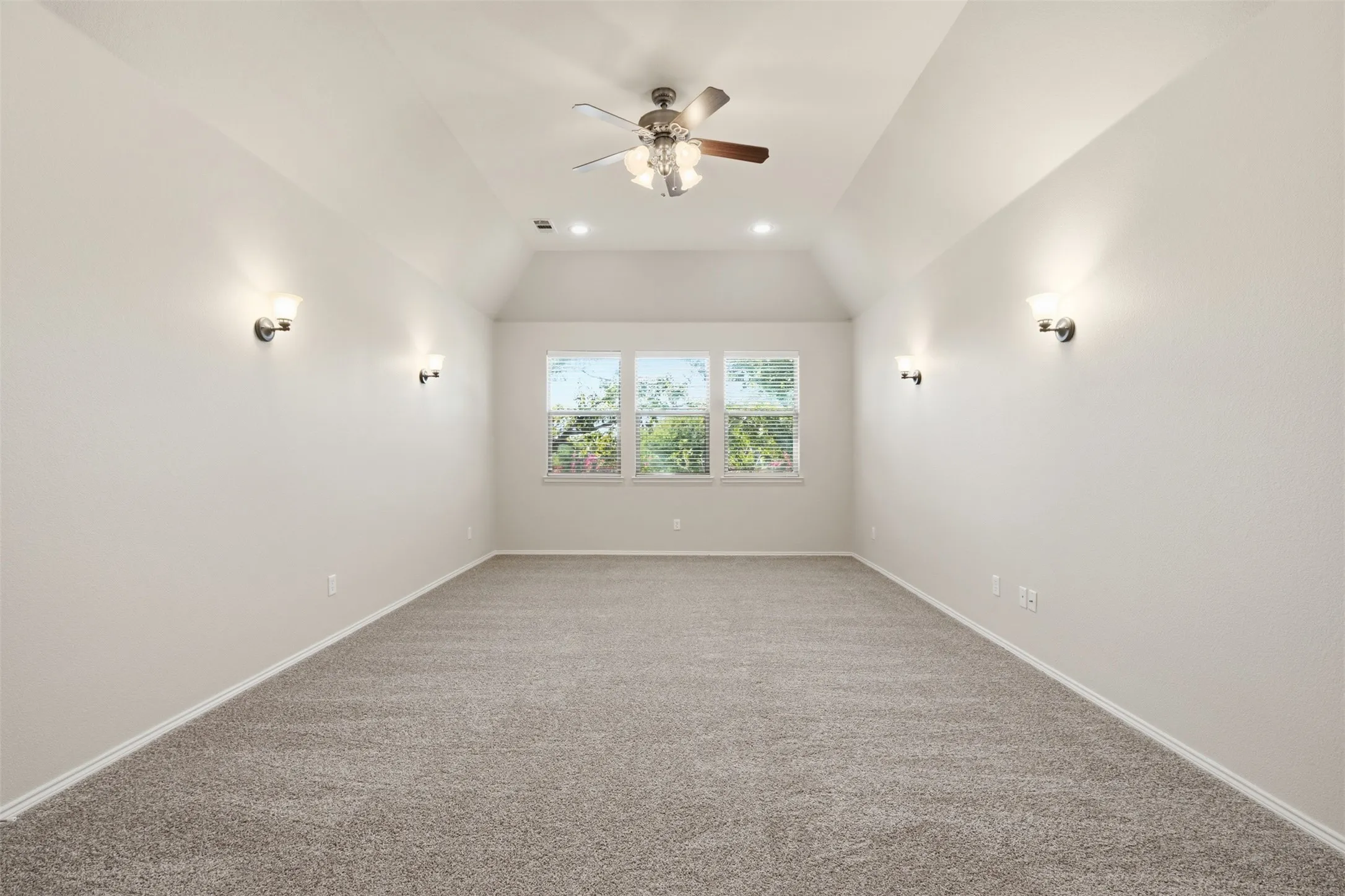 Vaulted ceiling with a ceiling fan, recessed lighting, wall sconces, triple windows, and carpet flooring