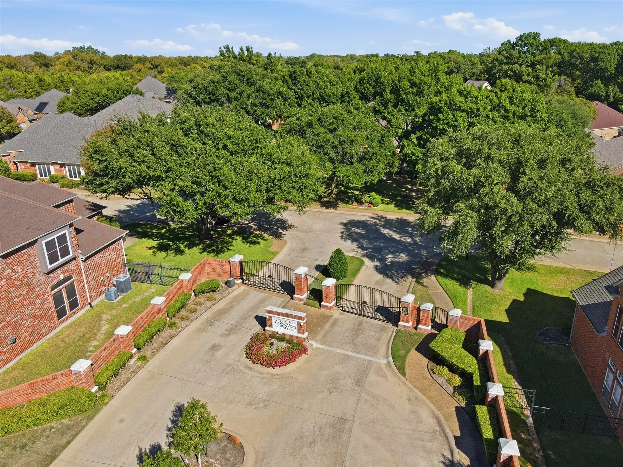 Gated community entrance with brick pillars, wrought iron gates, and a landscaped central island