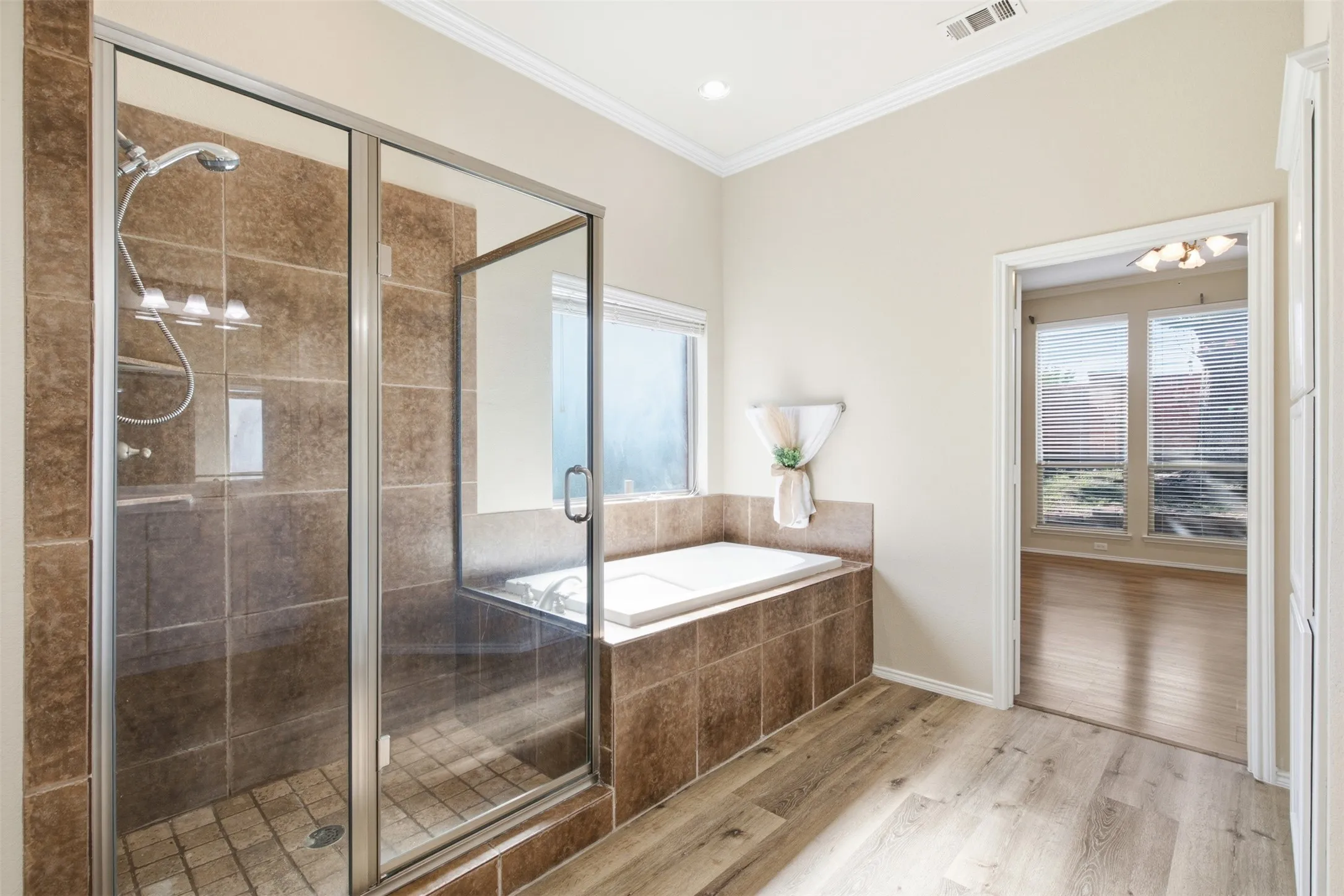 Glass-enclosed shower with tile surround, separate built-in soaking tub, wood-finish flooring, and crown molding