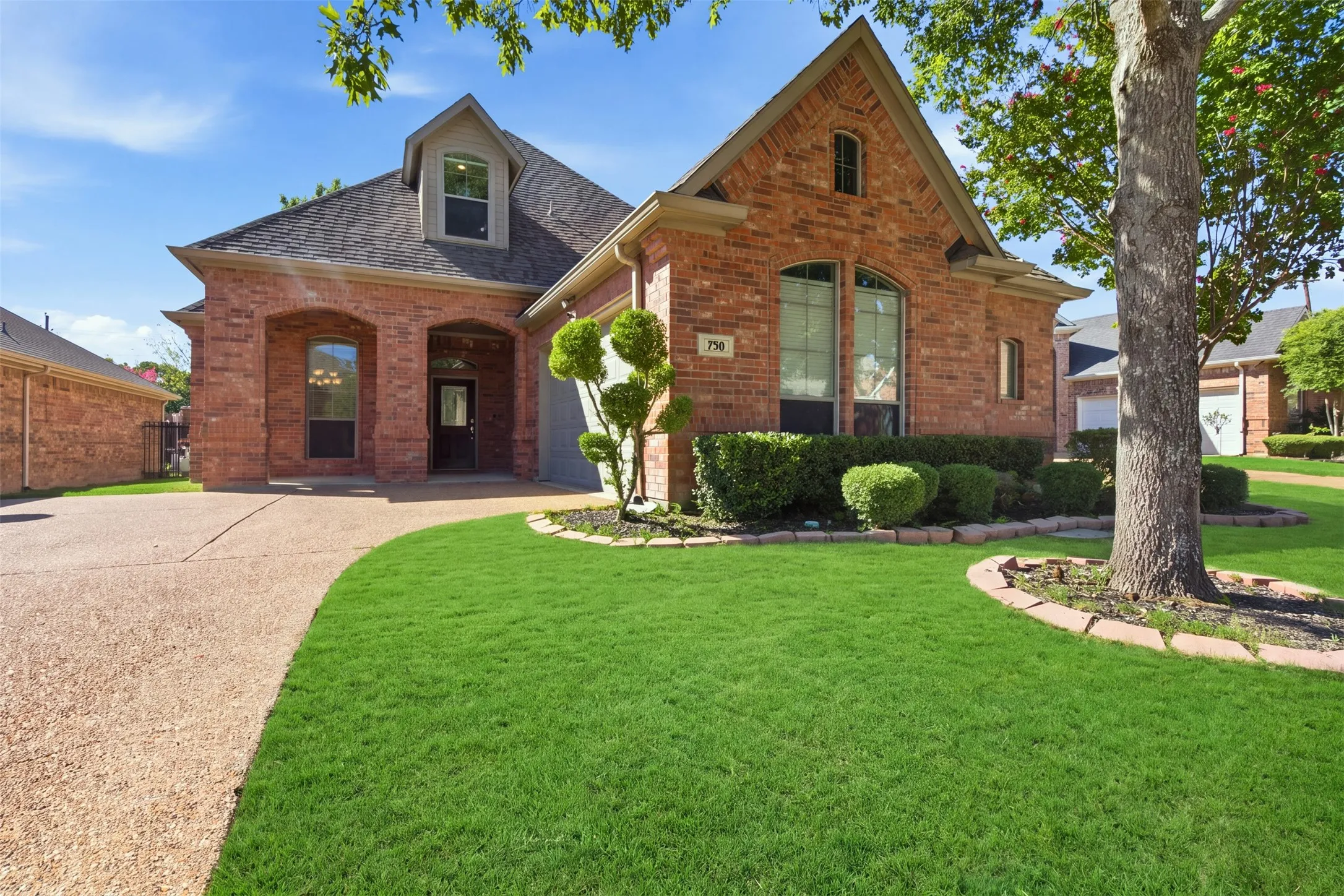 Brick exterior with arched entryways, dormer window, and a gabled roofline. Green enhancement to lawn.