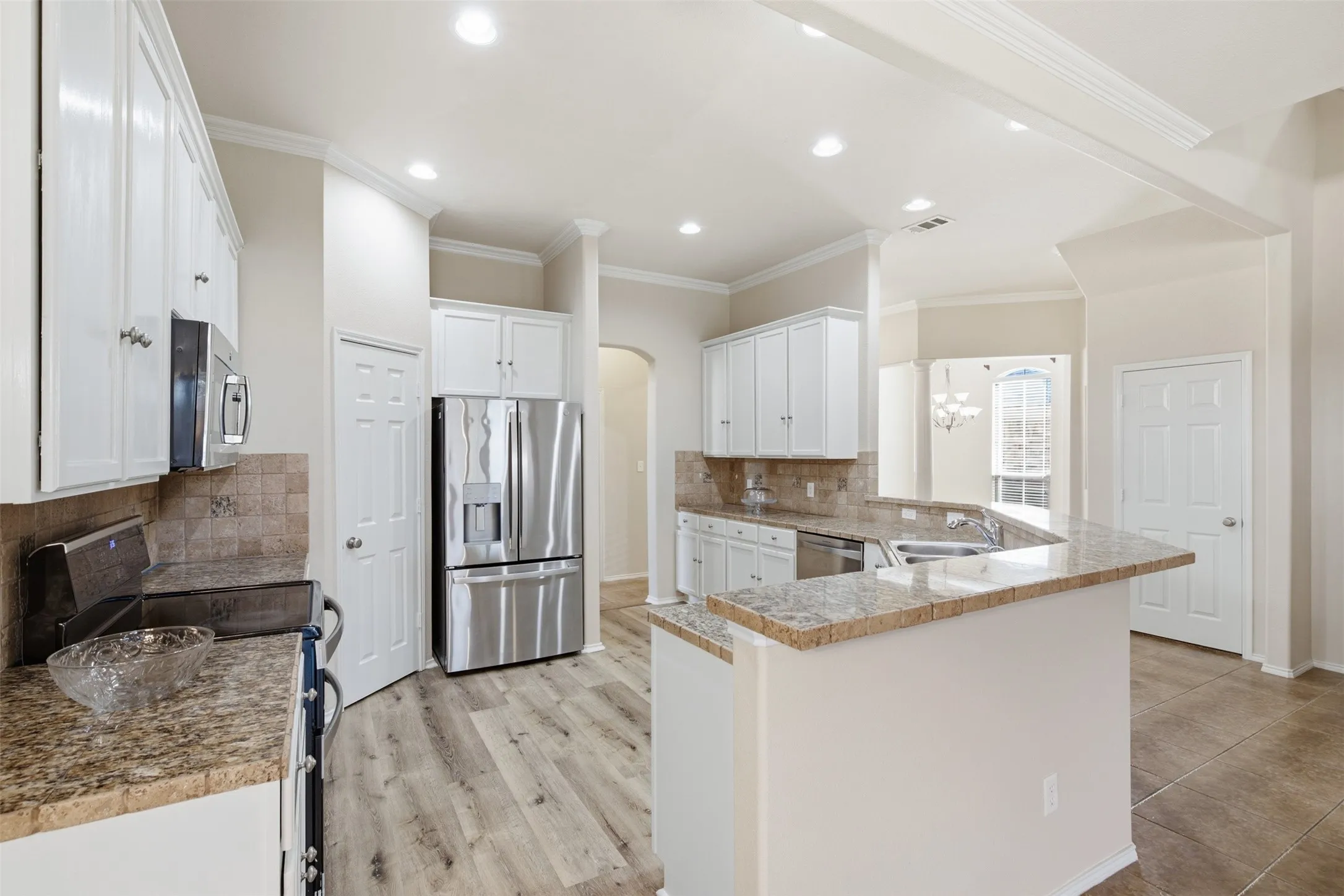 Kitchen featuring white cabinetry, granite countertops, stainless steel appliances, wood-finish flooring, and crown molding