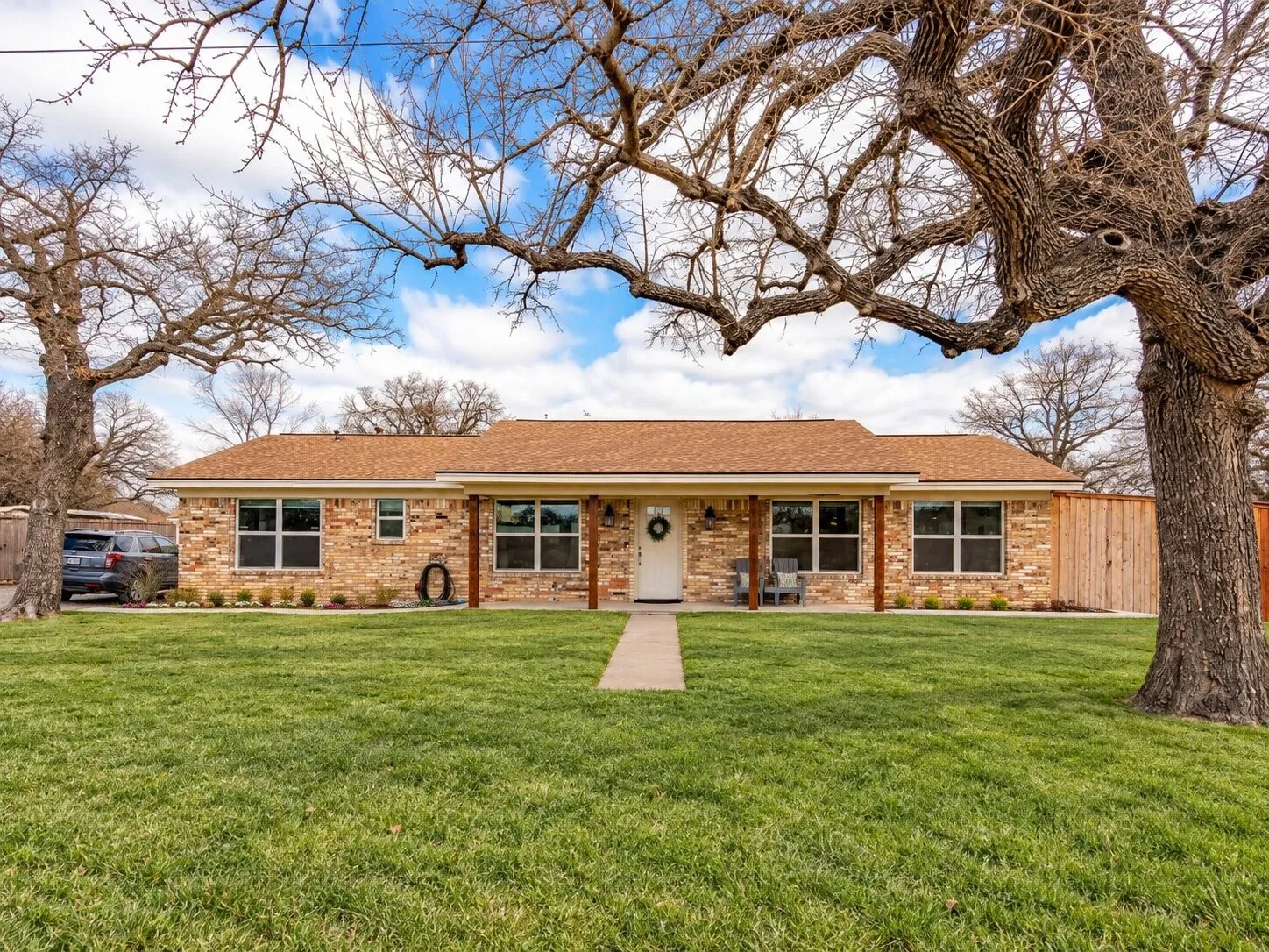 Brick exterior with a brown shingle roof, covered front porch, and a concrete walkway