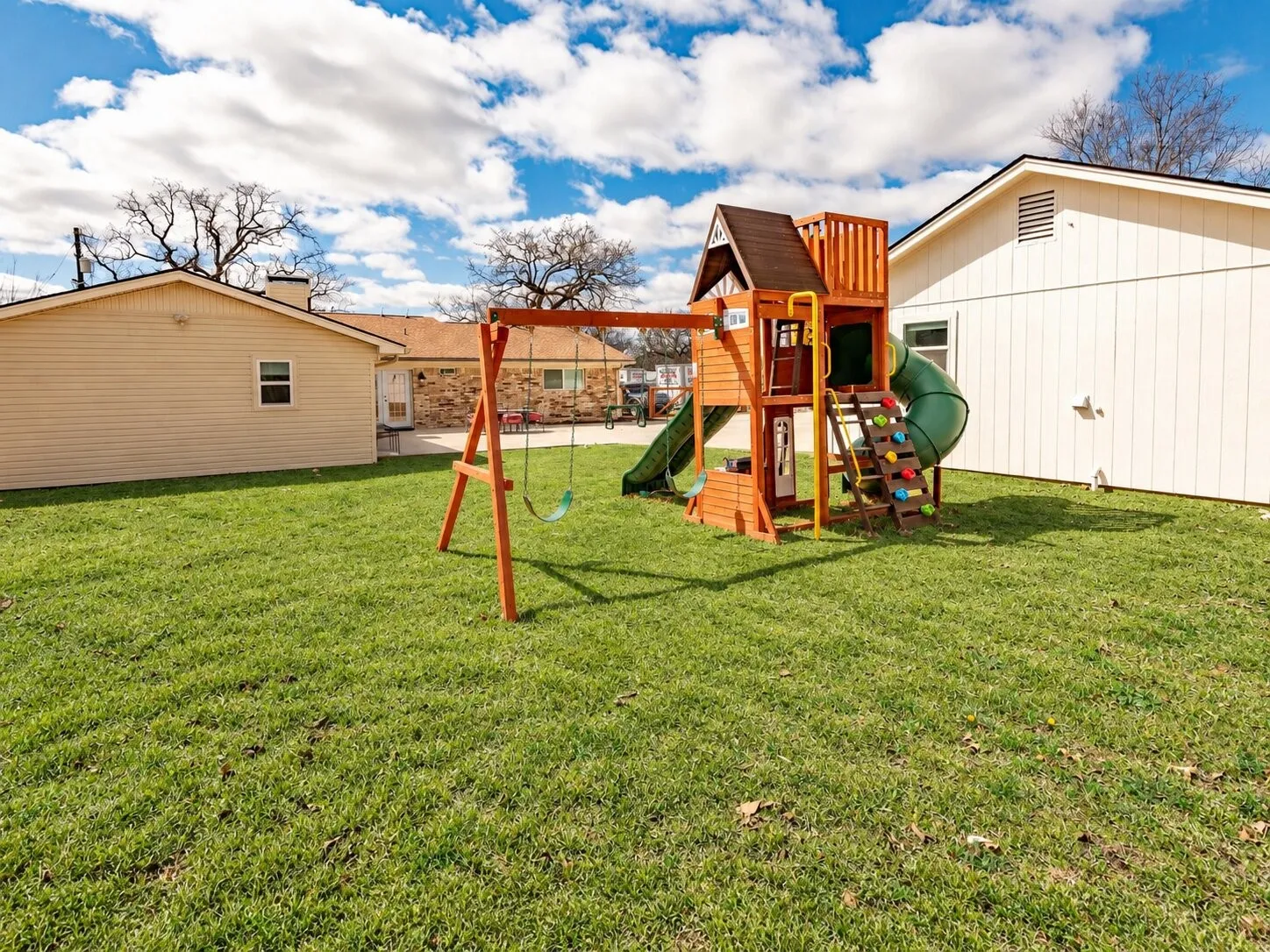 Expansive green lawn featuring a wooden playset with swings, slide, and climbing wall