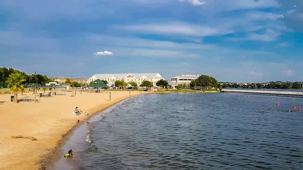 Waterfront property with sandy shoreline, mature trees, and a distant pier