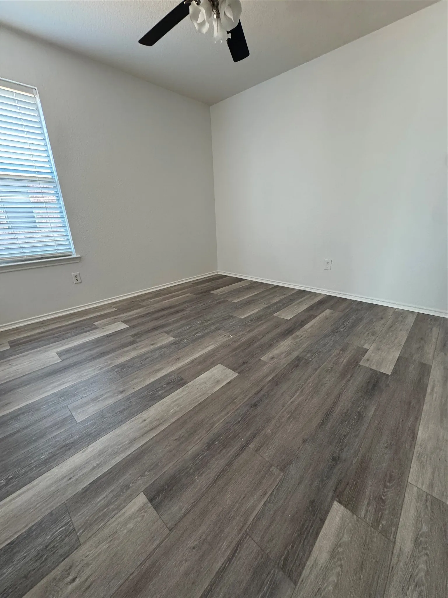 Wood-finish plank flooring, ceiling fan, white baseboards, and window with blinds