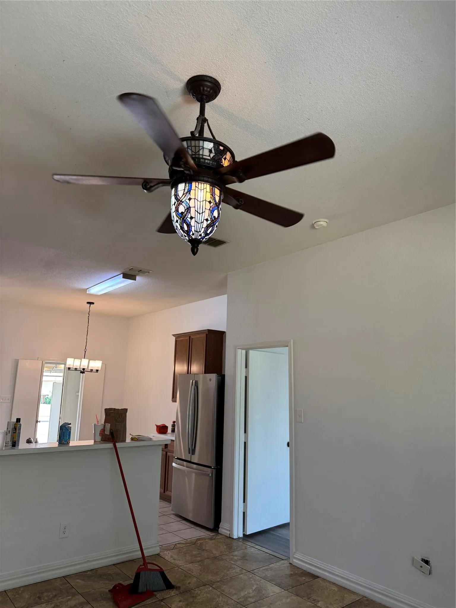 Decorative ceiling fan, from living room to kitchen with stainless steel refrigerator, dark wood-finish cabinetry, tile flooring, and white walls
