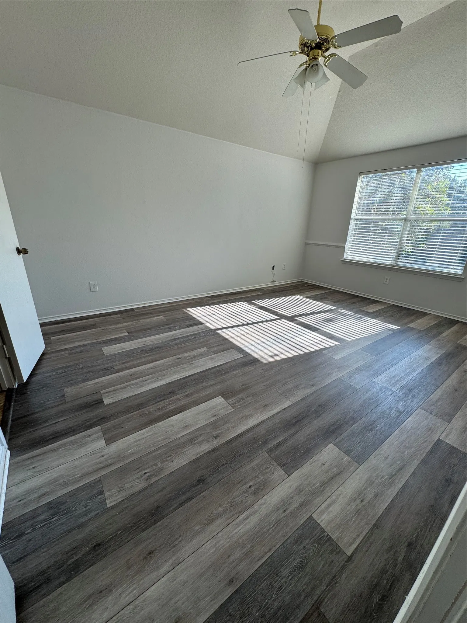 Vaulted ceiling with a ceiling fan, dual windows with blinds, and wood-finish flooring