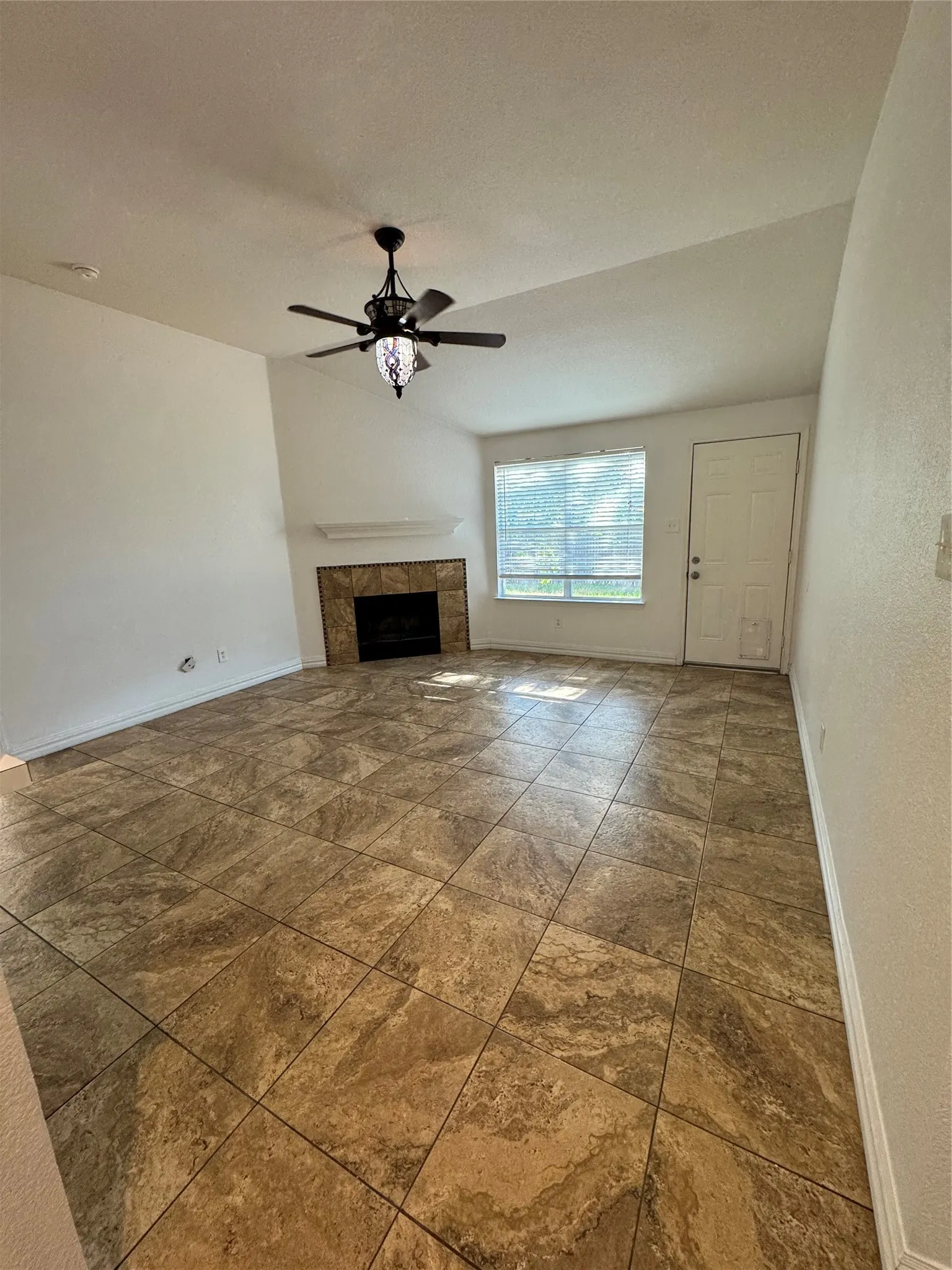 Spacious living area featuring tile flooring, a fireplace with a tiled surround, a white mantel, and a ceiling fan with integrated lighting