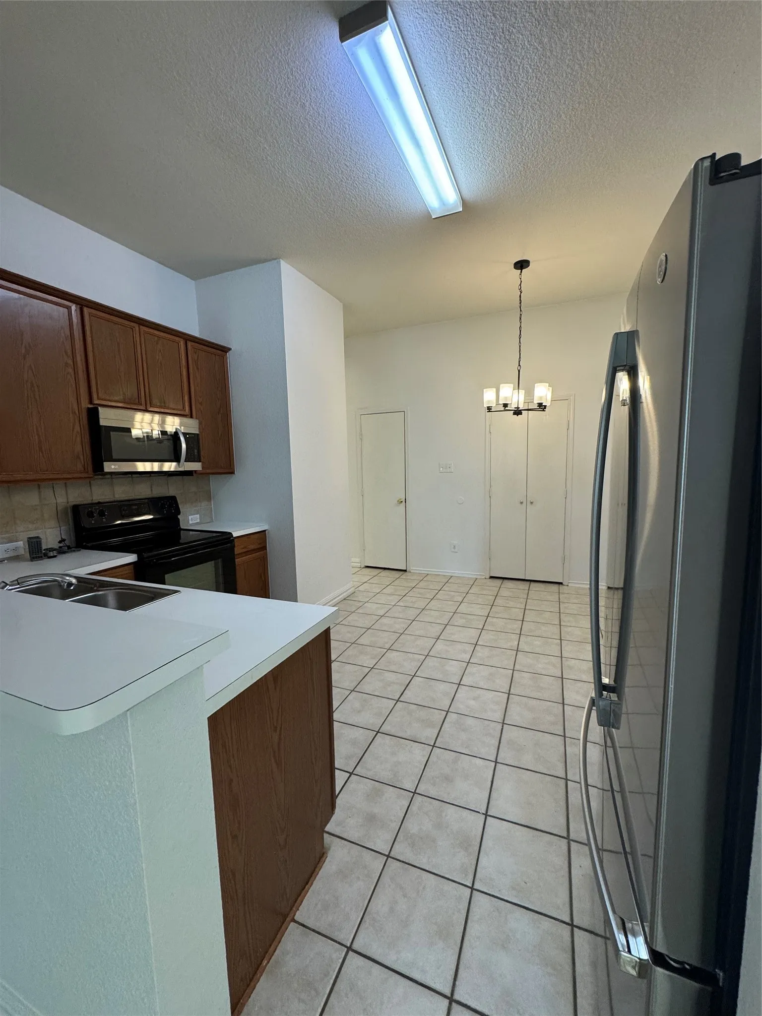 Tile flooring throughout, wood-finish cabinetry, stainless steel appliances, and a modern chandelier