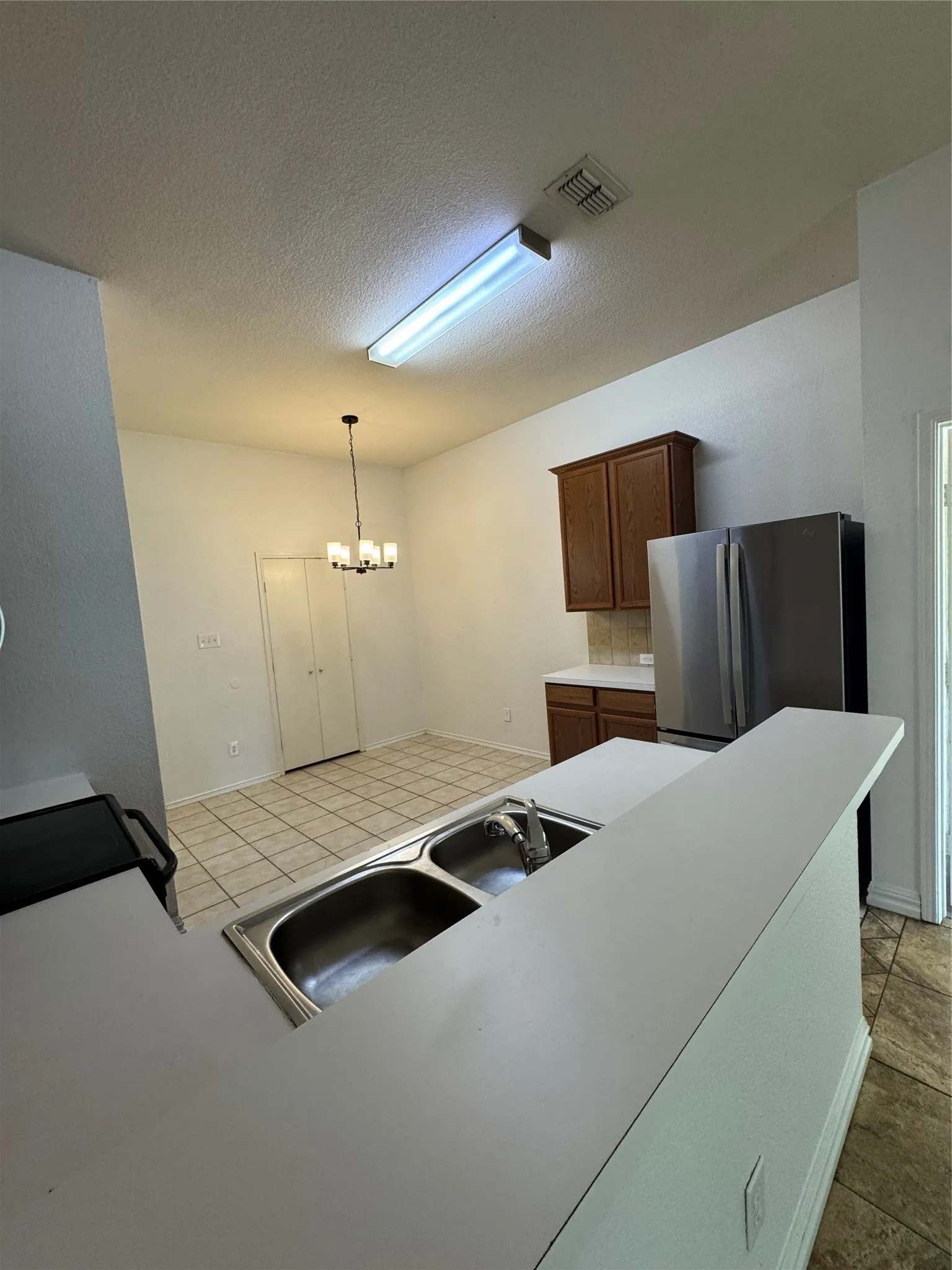 Kitchen featuring a double stainless steel sink, light-toned countertops, and wood-finish cabinetry