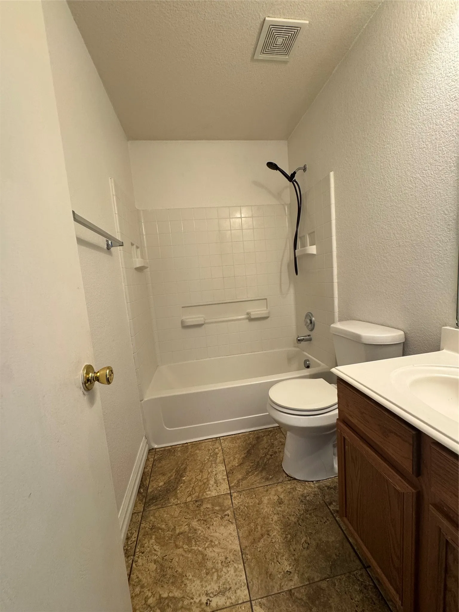 Bathroom featuring a bathtub with shower, white tile surround, a single vanity with wood-finish cabinetry, and textured floor tiling