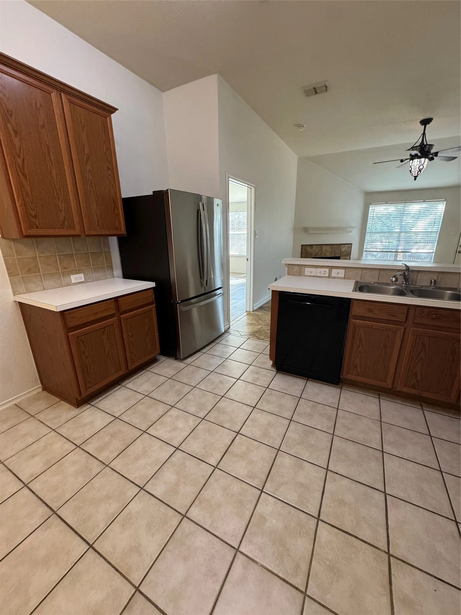 Kitchen featuring tile flooring, wood-finish cabinetry, stainless steel refrigerator, and a built-in black dishwasher