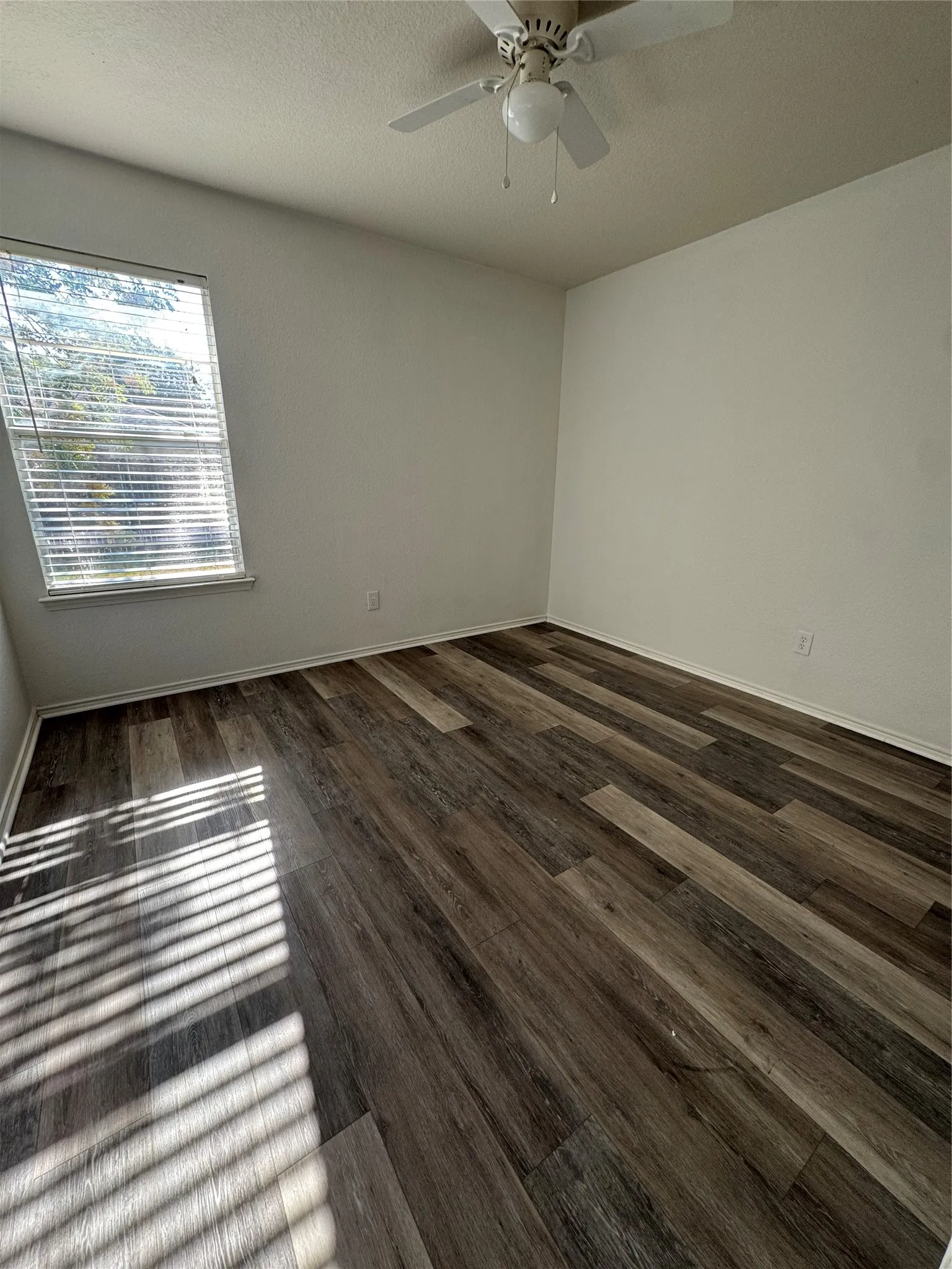 Wood-finish flooring, ceiling fan with integrated lighting, and a window with horizontal blinds