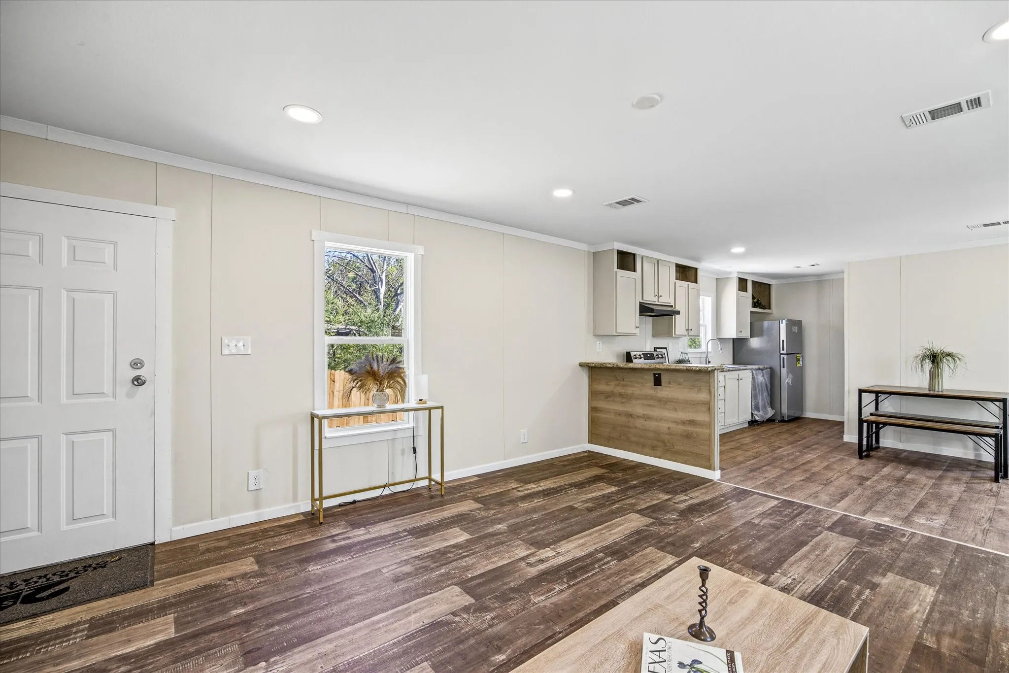 Expansive wood-finish flooring throughout, recessed ceiling lighting, and a kitchen featuring light cabinetry, a built-in range hood, and a functional breakfast bar with an integrated wood-finish panel