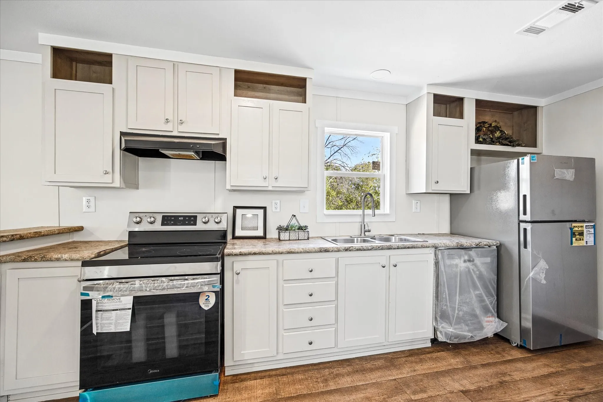 Kitchen featuring wood-finish flooring, white cabinetry, a double basin sink with a high-arc faucet, a stainless steel electric range, and a stainless steel refrigerator