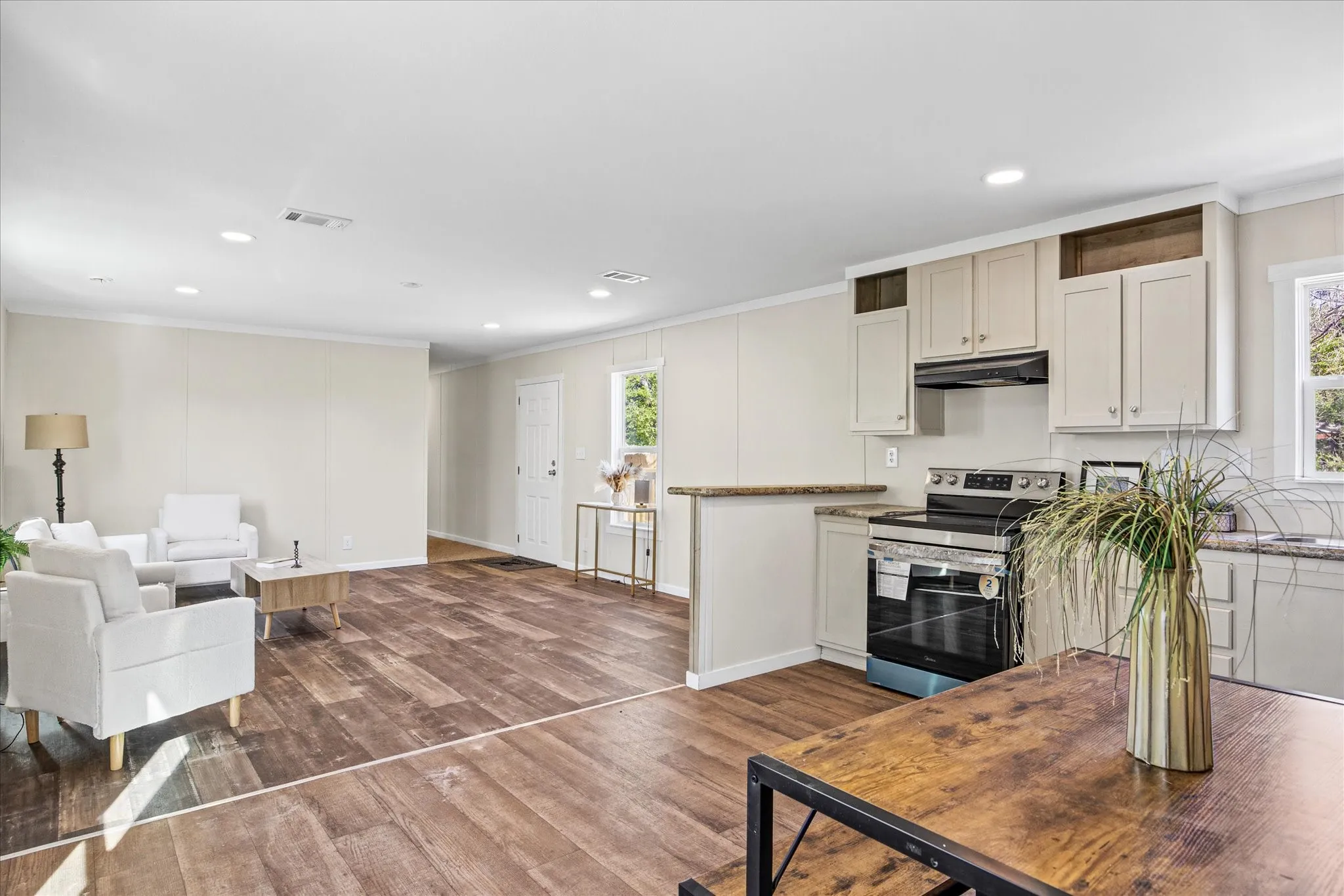 Open-concept living space featuring wood-finish flooring, recessed lighting, and a kitchen with light cabinetry and a stainless steel oven range
