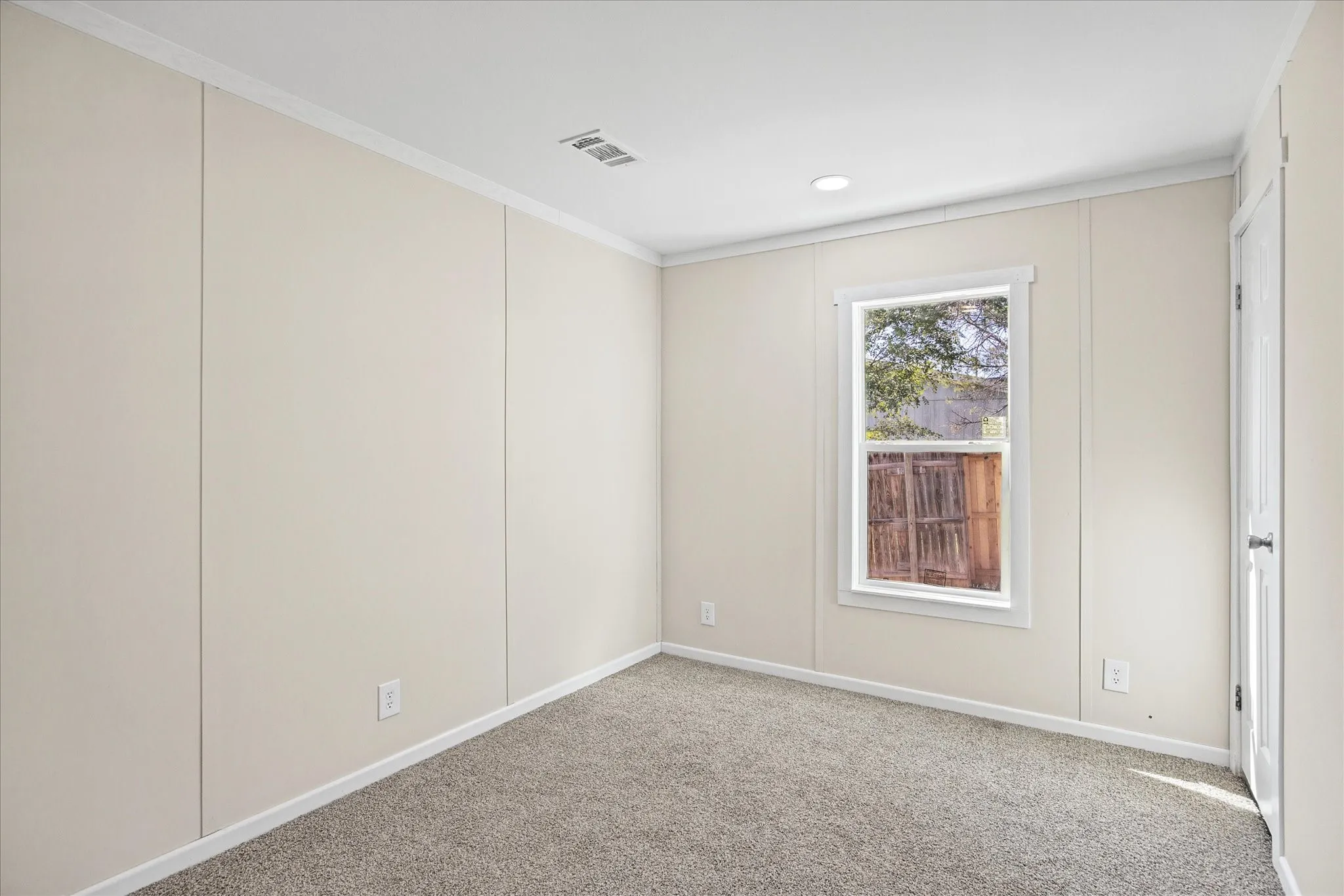 Recessed ceiling lighting, white crown molding, light neutral wall panels, gray carpet flooring, and a white framed window