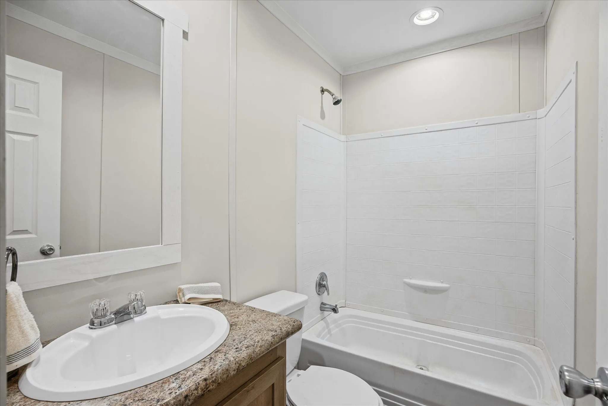 Bathroom featuring a single vanity with an oval sink, a stone-finish countertop, a framed mirror, and a tub-shower combination with a textured surround