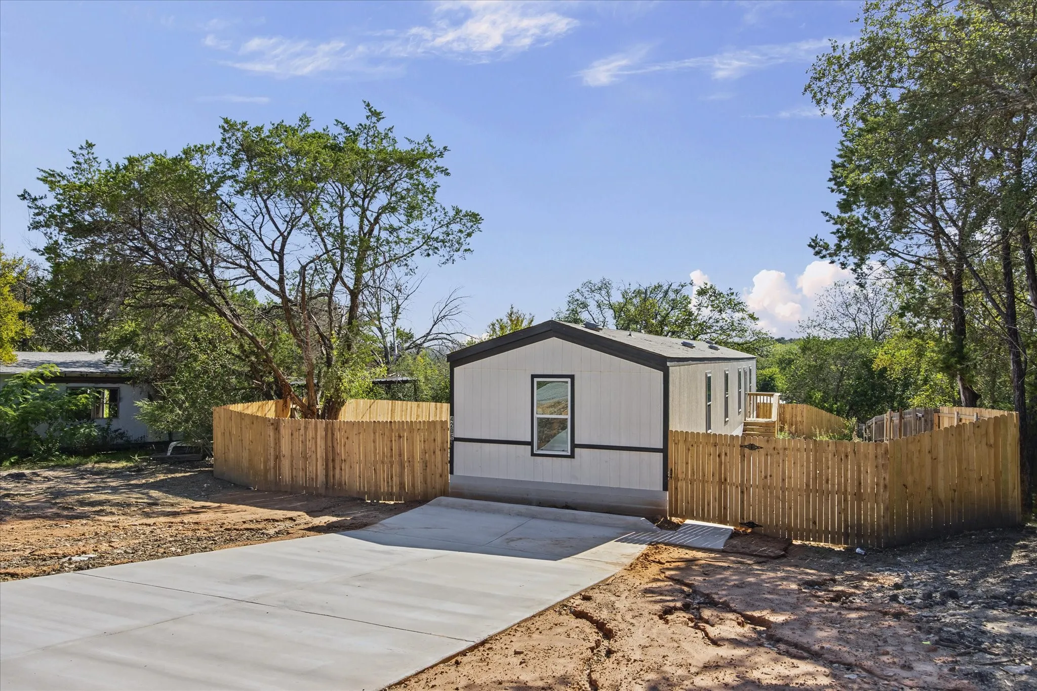 Contemporary residence featuring light-colored siding with dark trim, a dark roof, and a newly poured concrete driveway