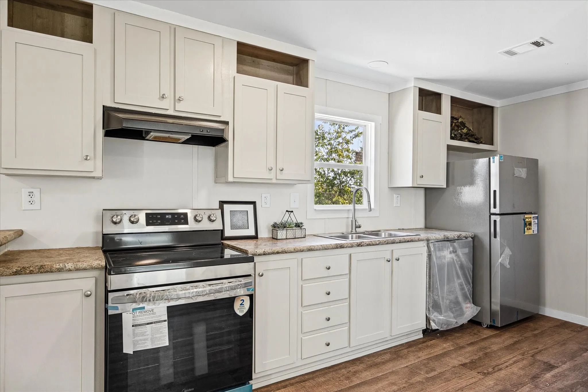 Kitchen featuring wood-finish flooring, white cabinetry, speckled countertops, stainless steel appliances, and a double basin sink with a chrome faucet