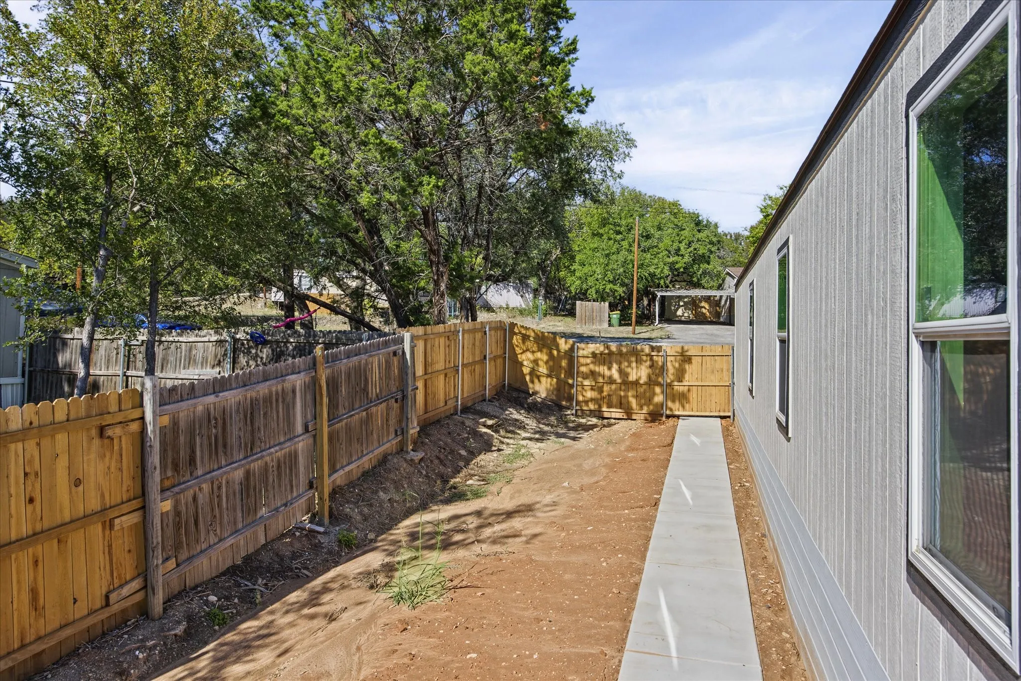 Side yard featuring a concrete walkway, light-colored vertical siding, and a wooden privacy fence