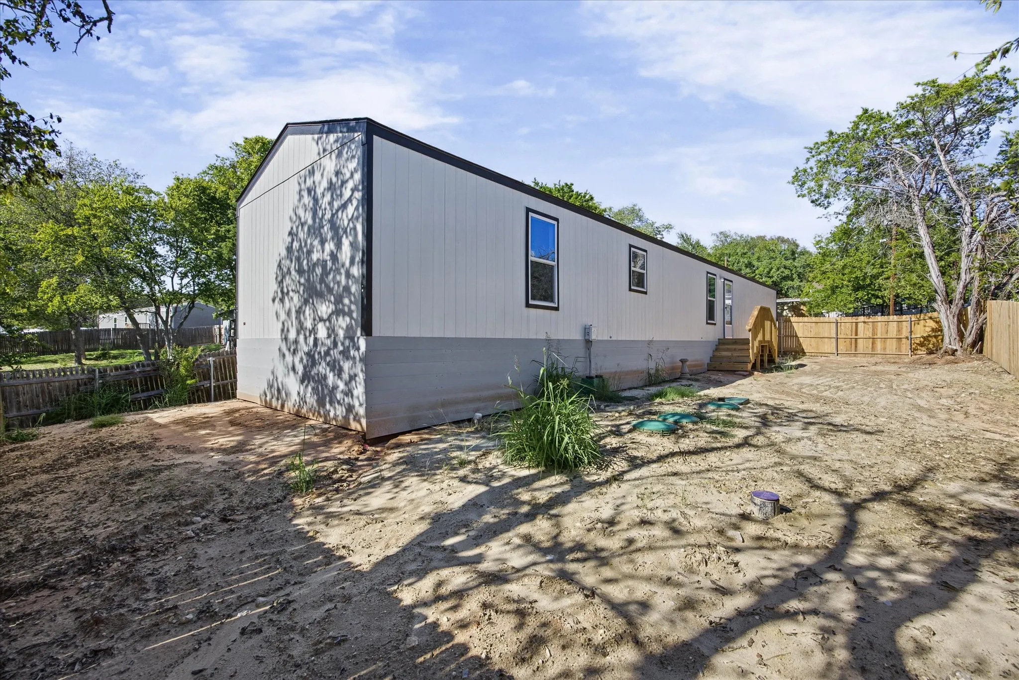 Neutral-toned siding with dark trim, multiple windows with dark frames, and a wooden rear entrance staircase