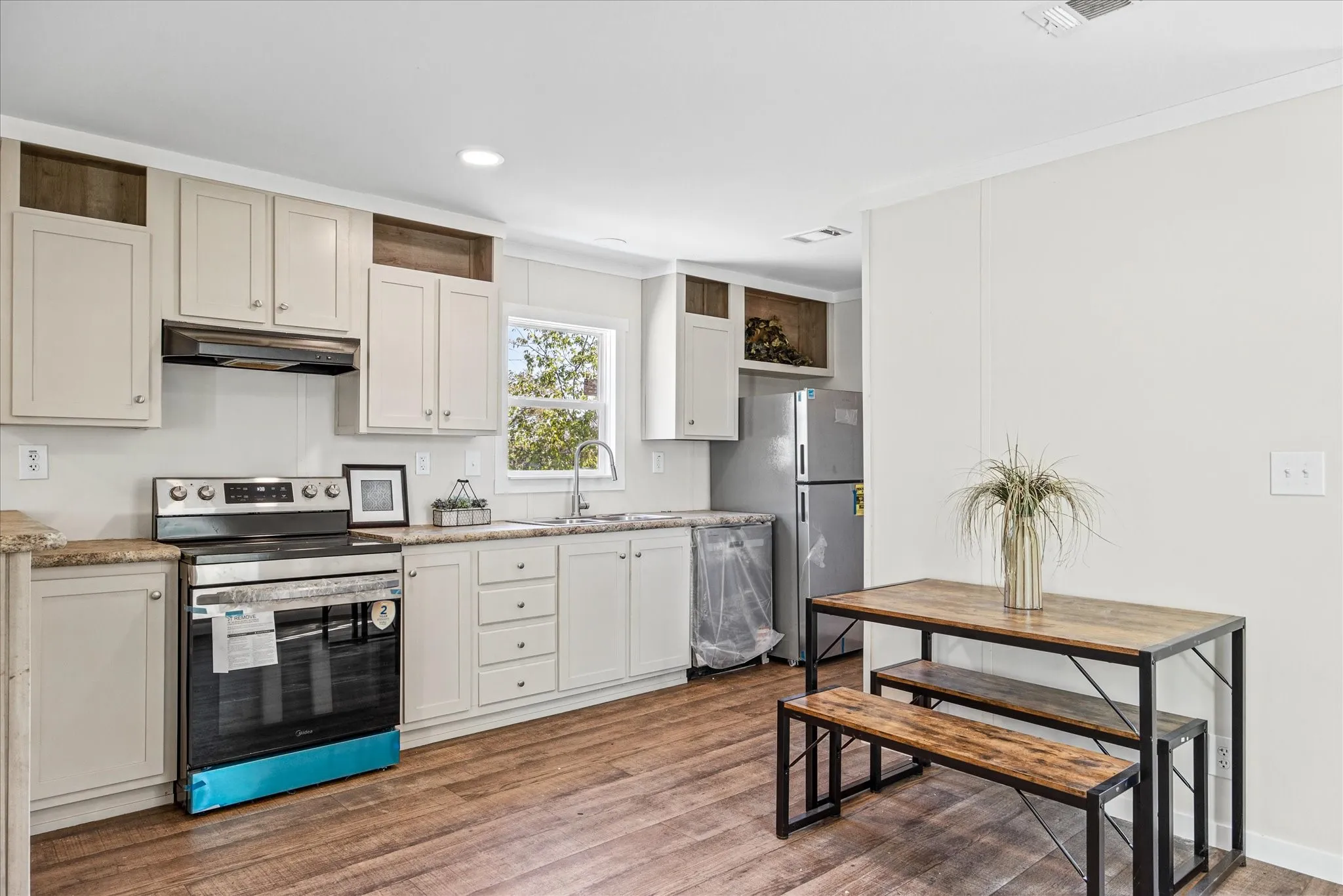 Kitchen featuring wood-finish flooring, light cabinetry, a stainless steel range, and a window above the sink
