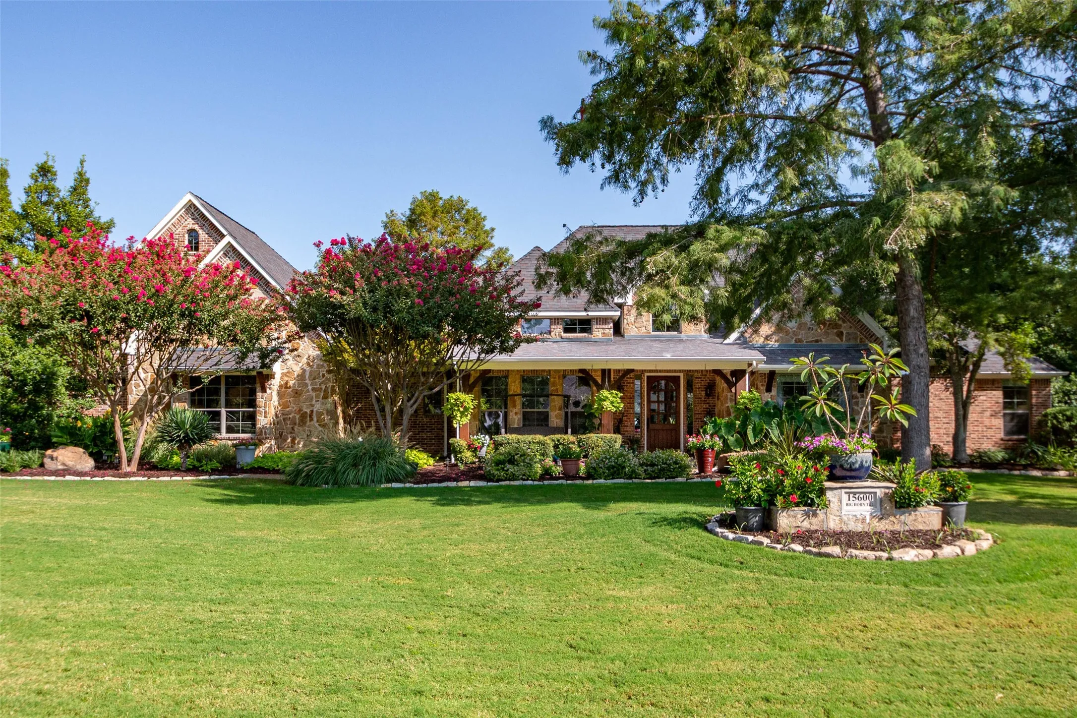 Stone and brick exterior with a front entry porch, mature landscaping, and a manicured lawn