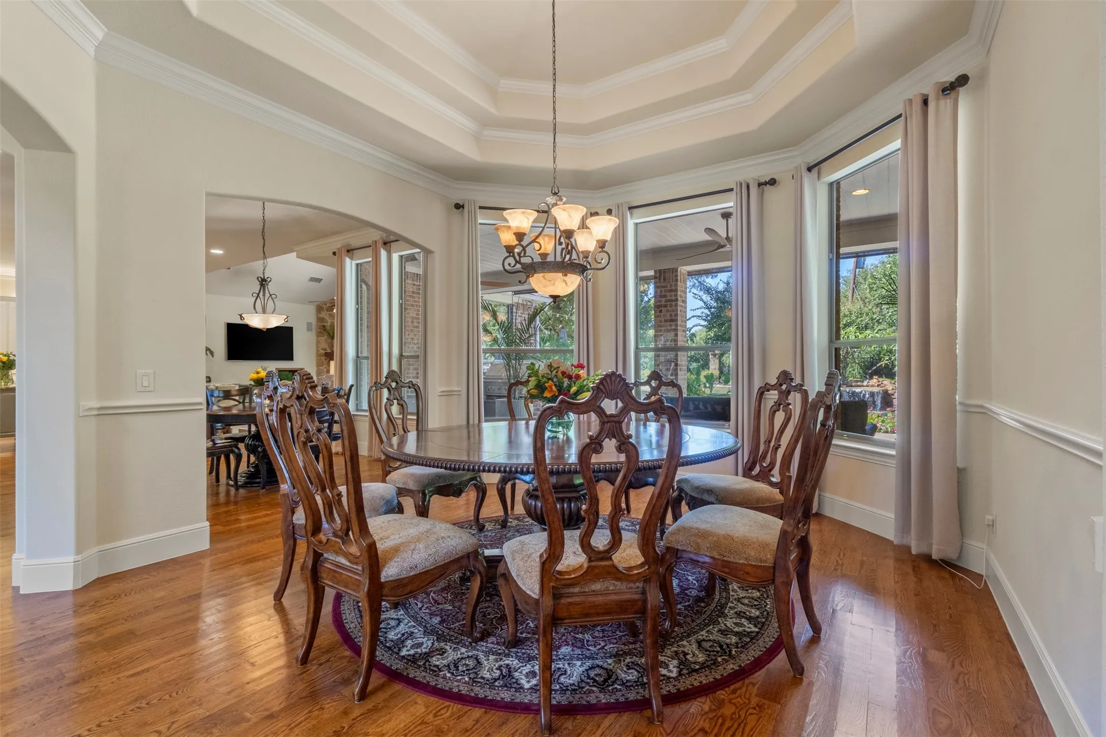 Hardwood flooring, arched entryway, tiered tray ceiling, decorative chandelier, and extensive crown molding