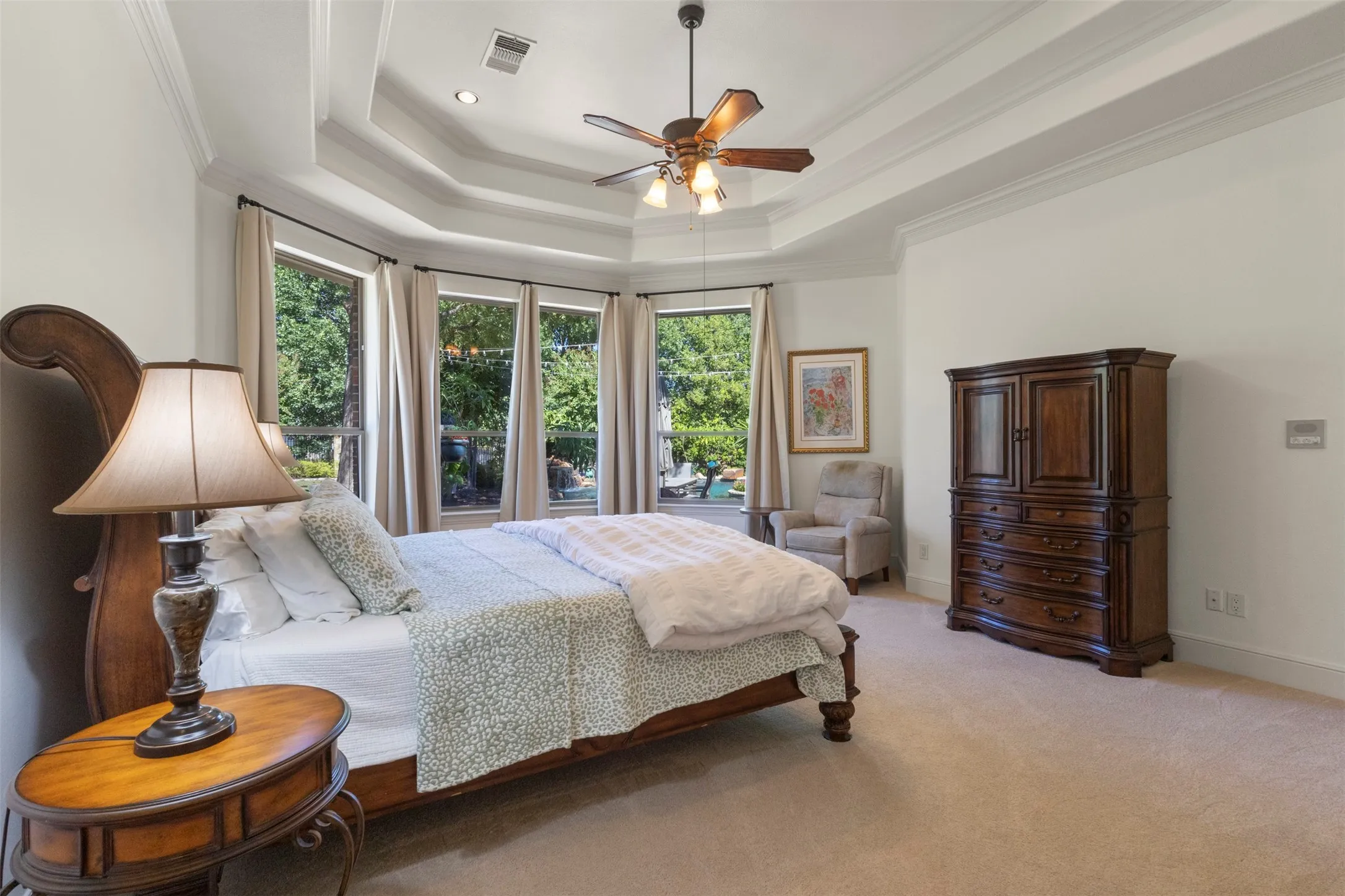 Tray ceiling with crown molding, ceiling fan, recessed lighting, bay windows with drapery, and carpeted flooring