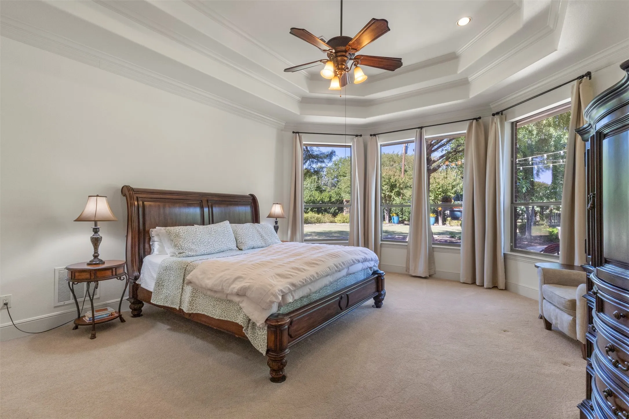 Tray ceiling with crown molding, ceiling fan, recessed lighting, wall-to-wall carpeting, and a bay window configuration