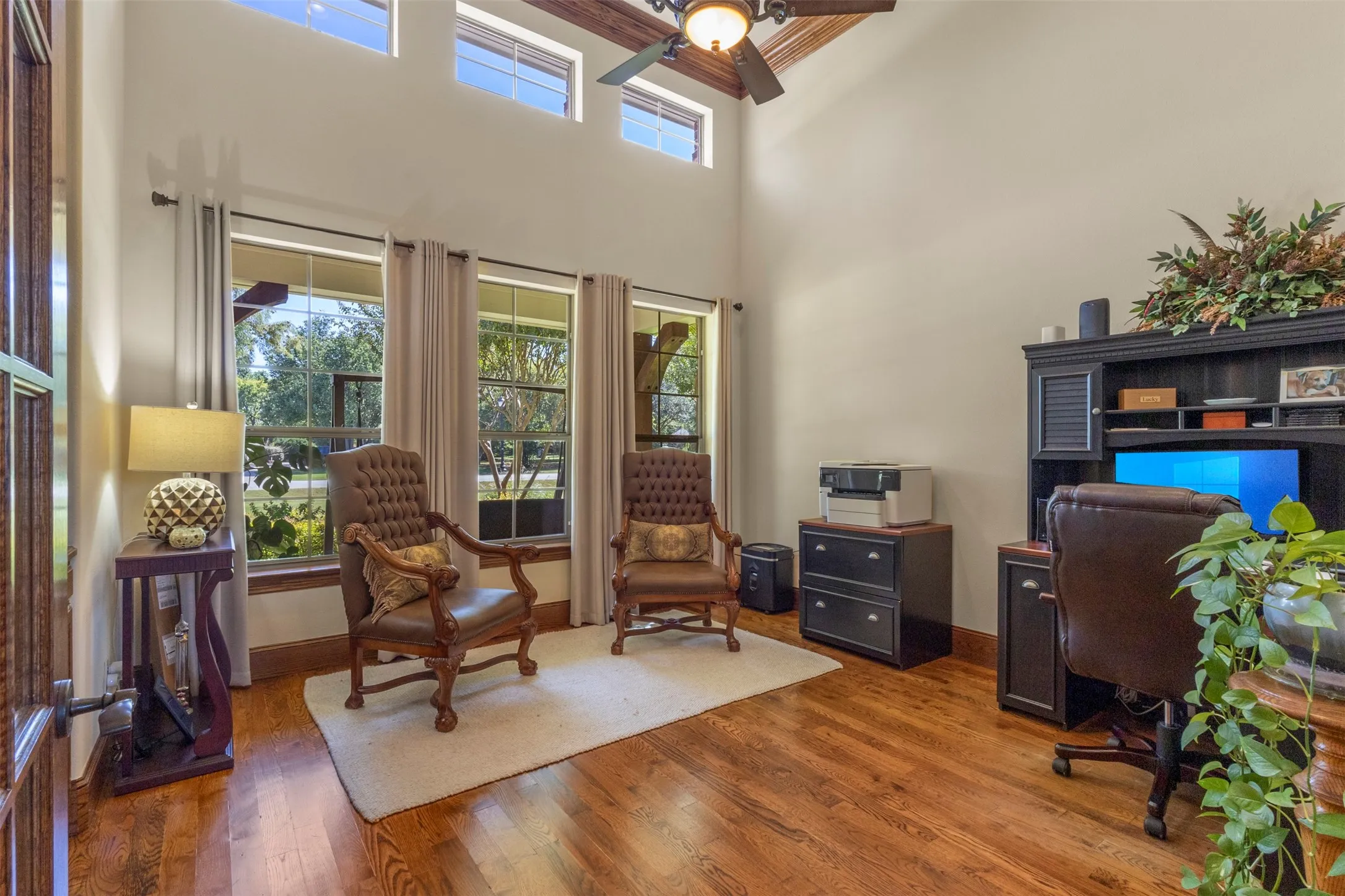 High ceilings with upper transom windows, wood-finish flooring, multiple large windows, and a built-in dark wood desk unit