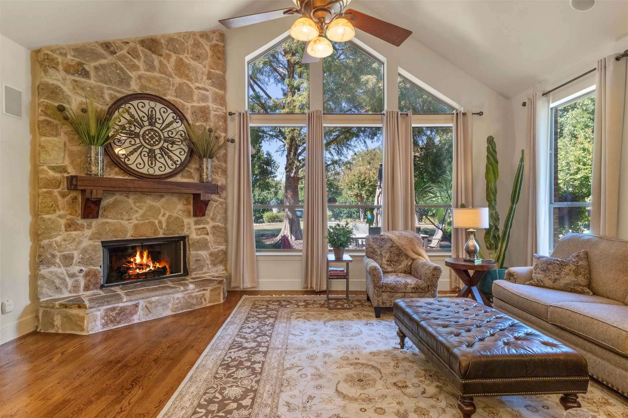 Stone-clad fireplace with wood mantel, vaulted ceiling, wood-finish flooring, and expansive windows